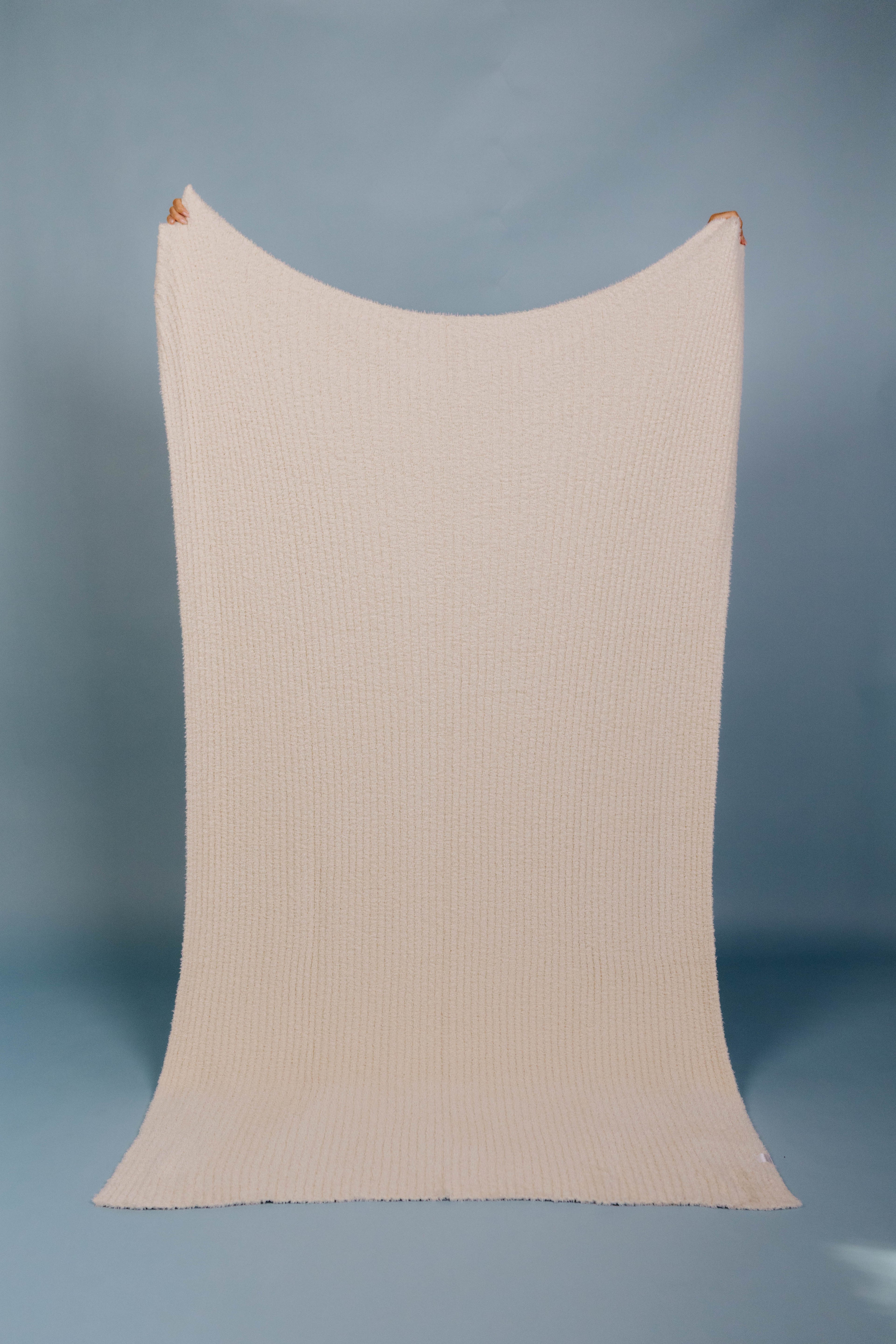 Beige ribbed blanket being held up on a blue background