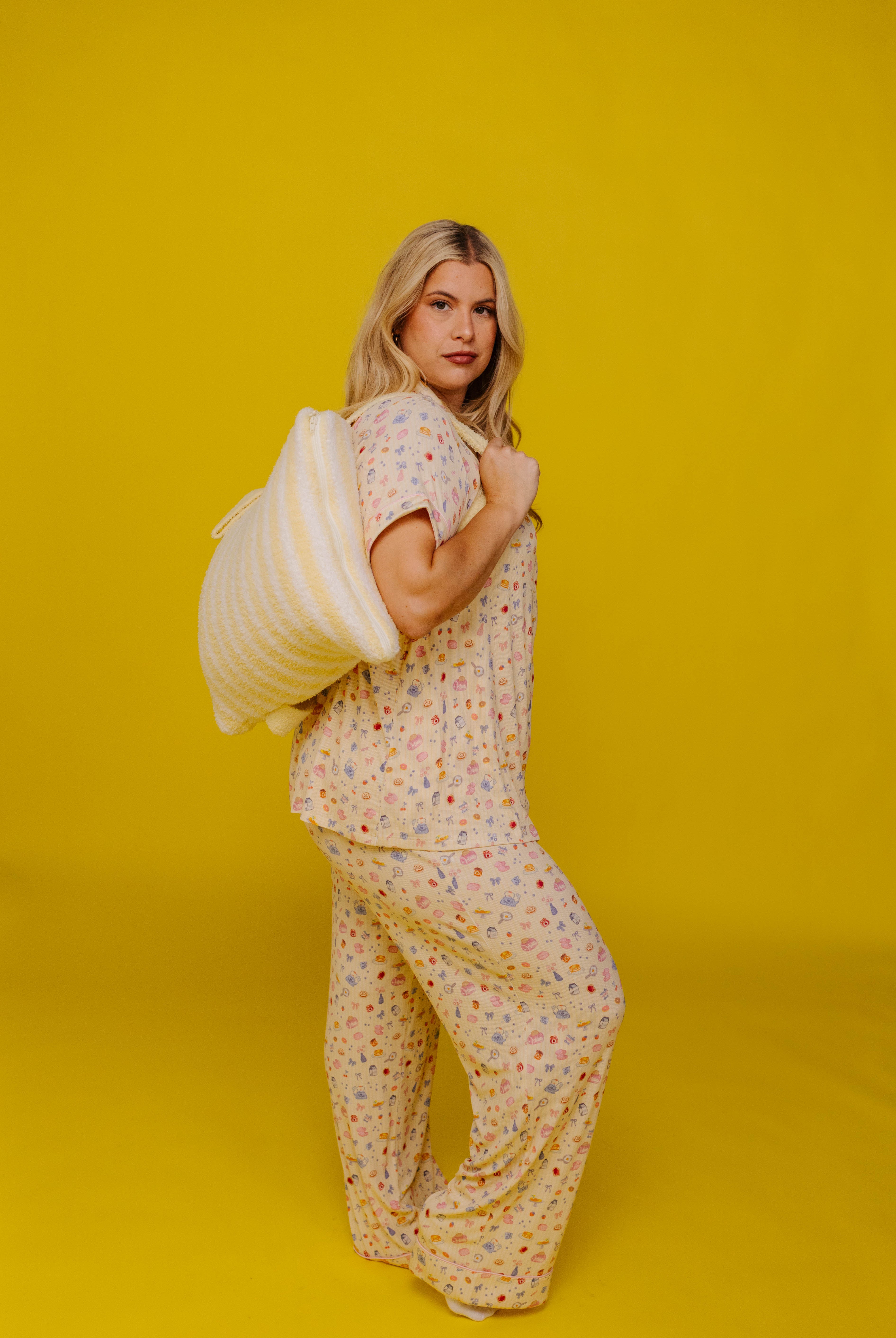 Woman in a brunch pj holding a white and yellow bag against a yellow background