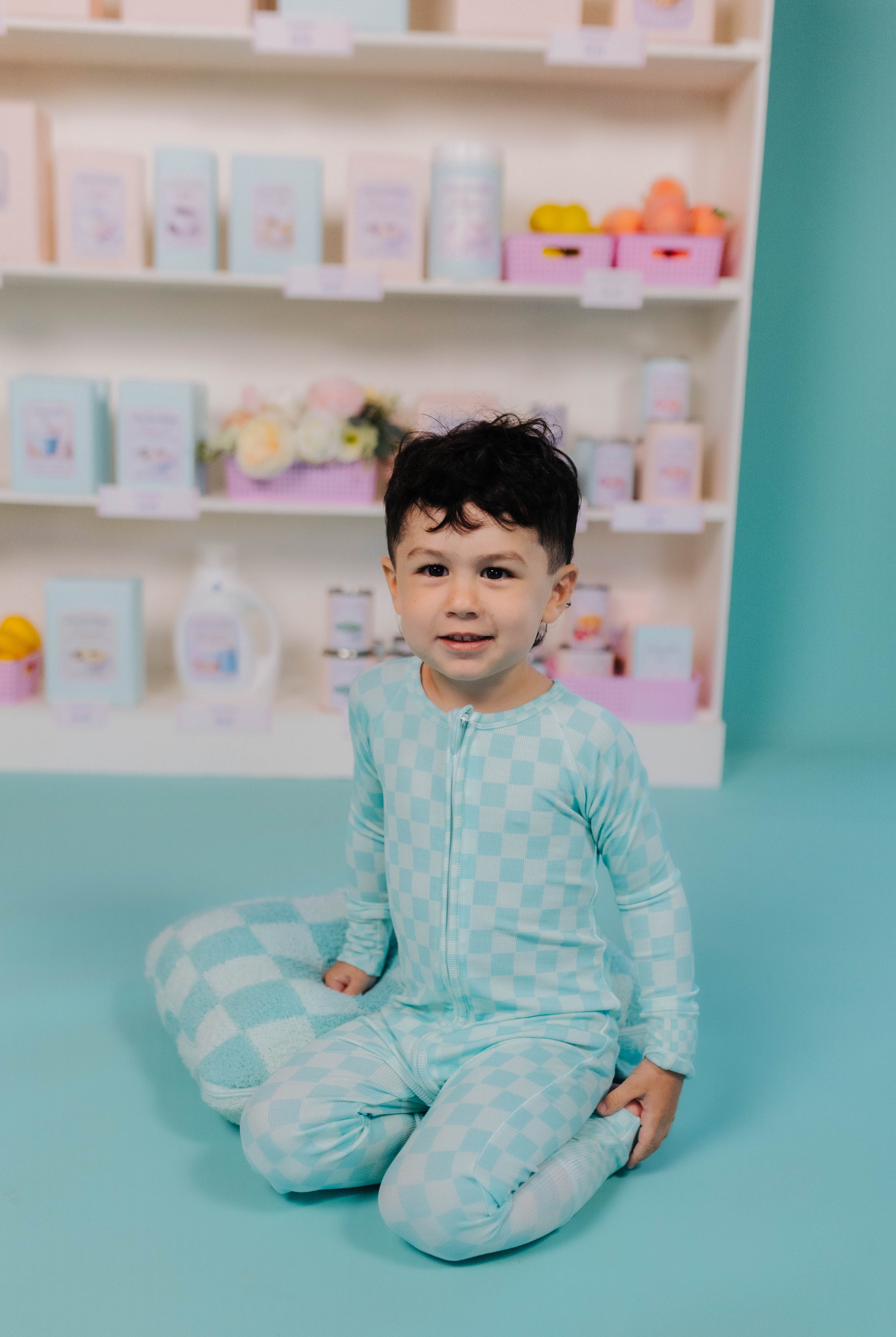 Child wearing a check onesie on a blue floor in front of shelves with products.