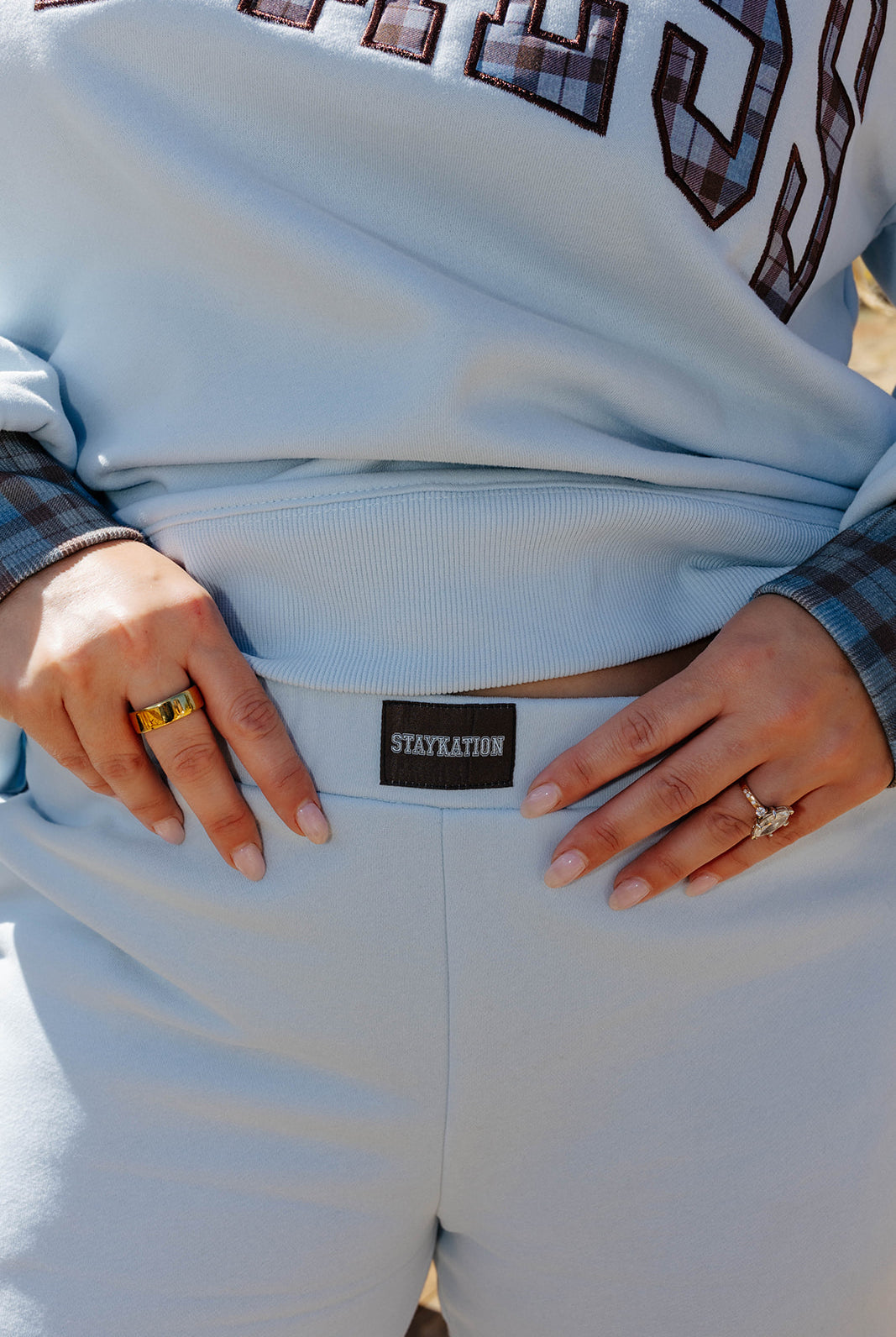 Close view of light blue sweatpants showing the waistband and Staykation label beneath a matching Hot Mess sweatshirt.