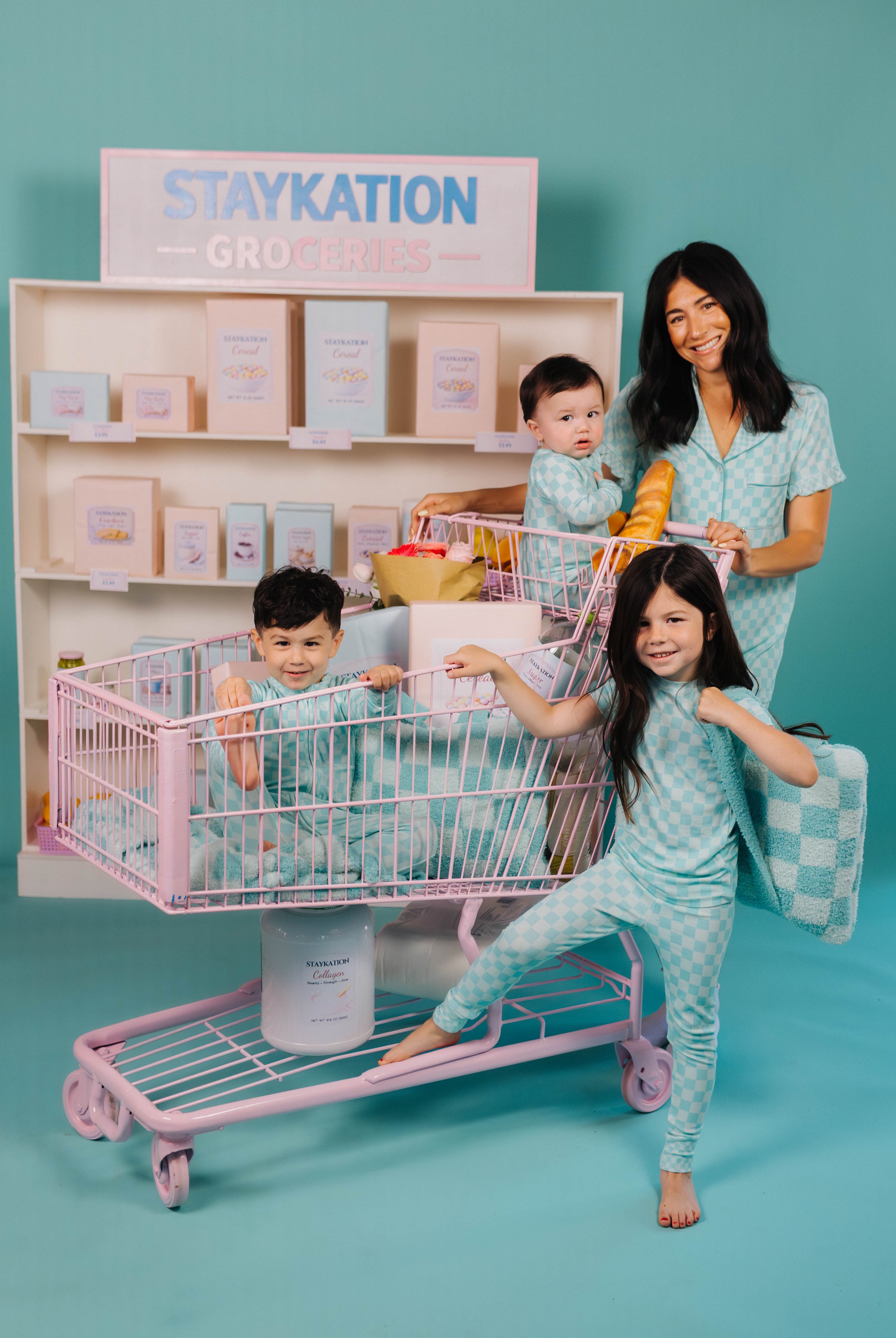 Family with children playing with a toy shopping cart against a teal background