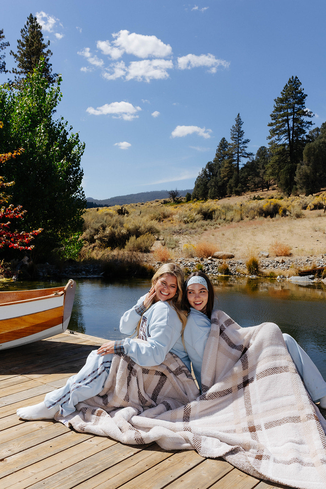 Three models seated together on a dock with the plaid blanket across their laps.