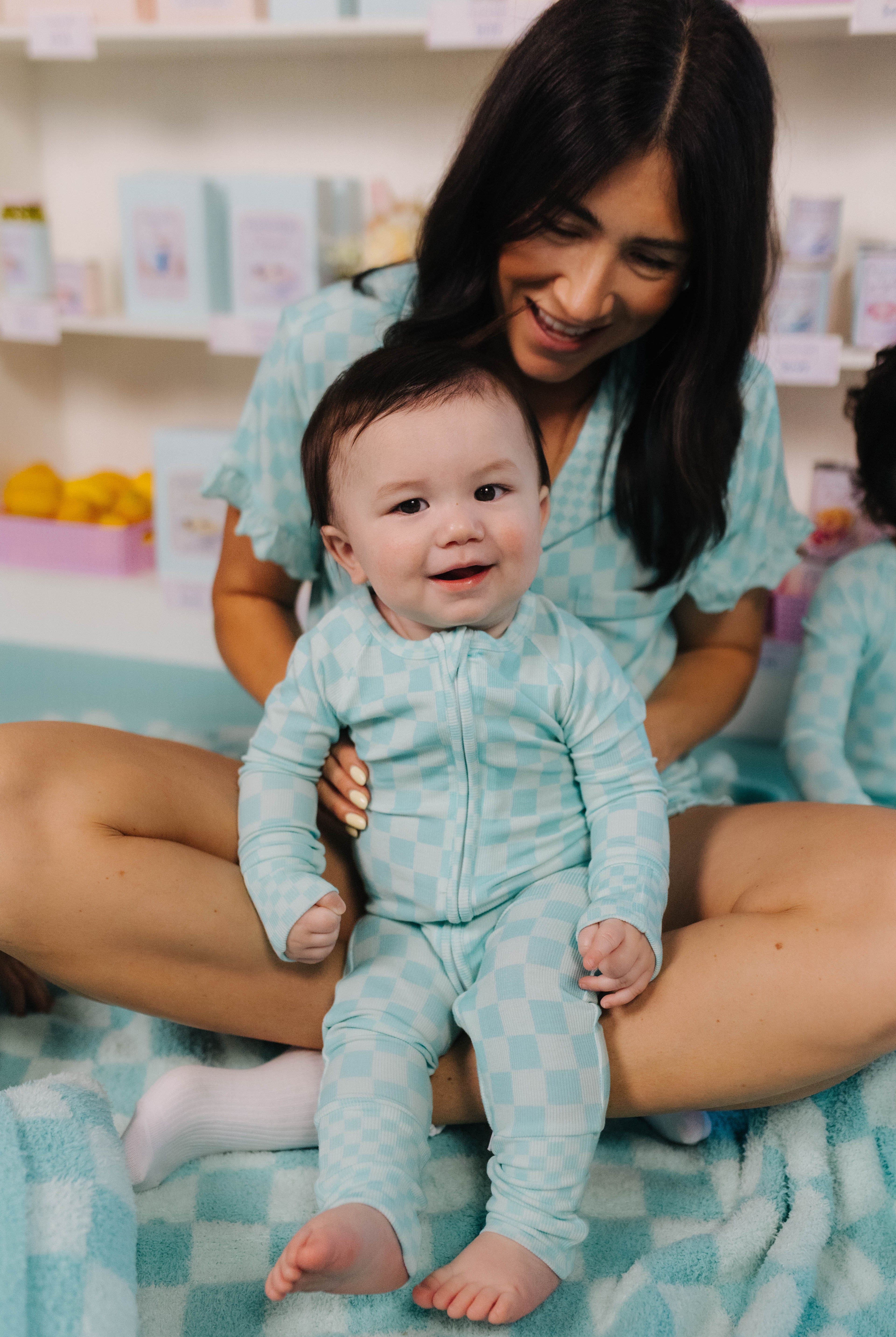 Woman holding a baby in matching teal outfits on a checkered blanket.