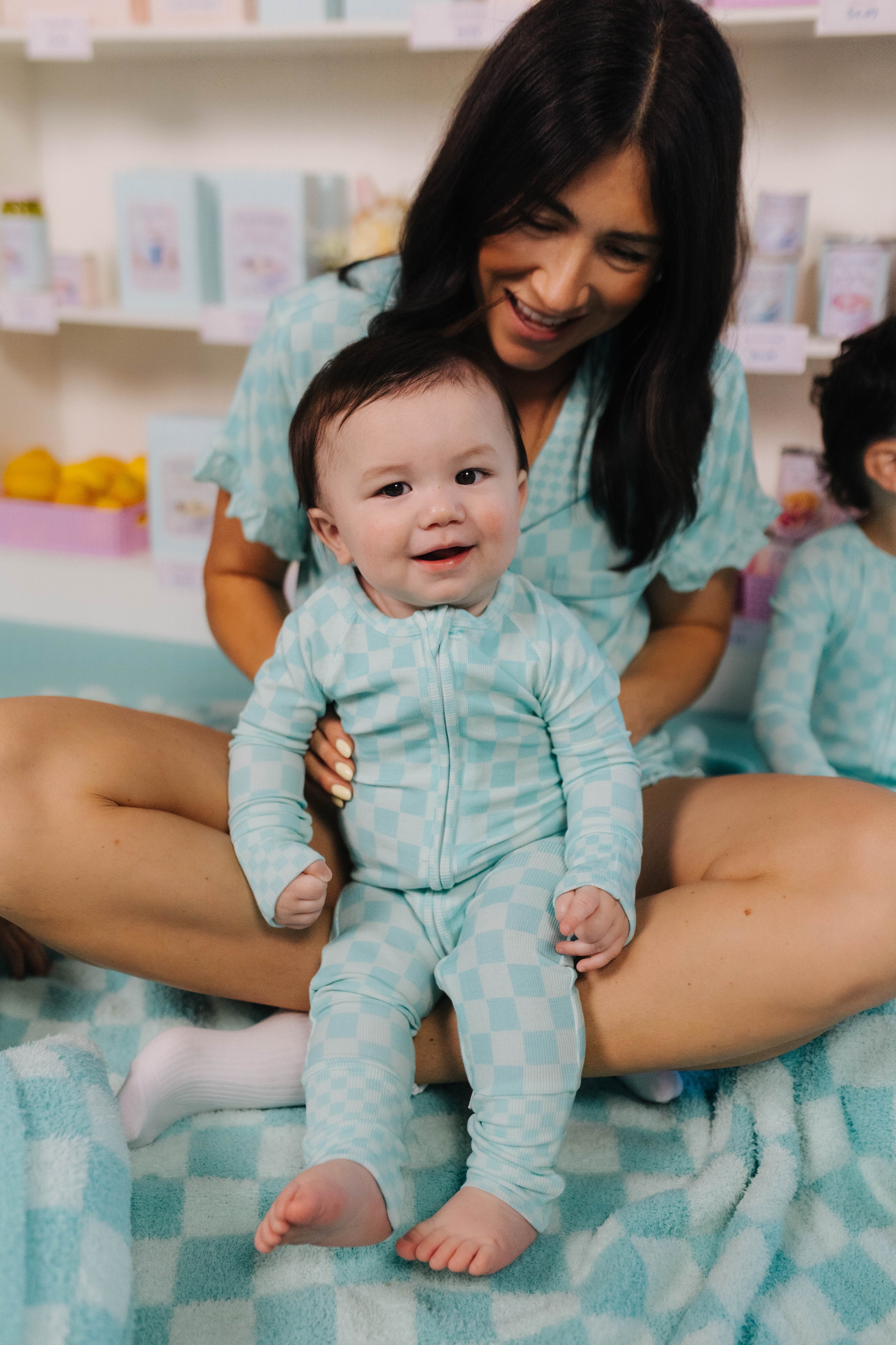 Woman holding a baby in matching teal outfits on a checkered blanket.