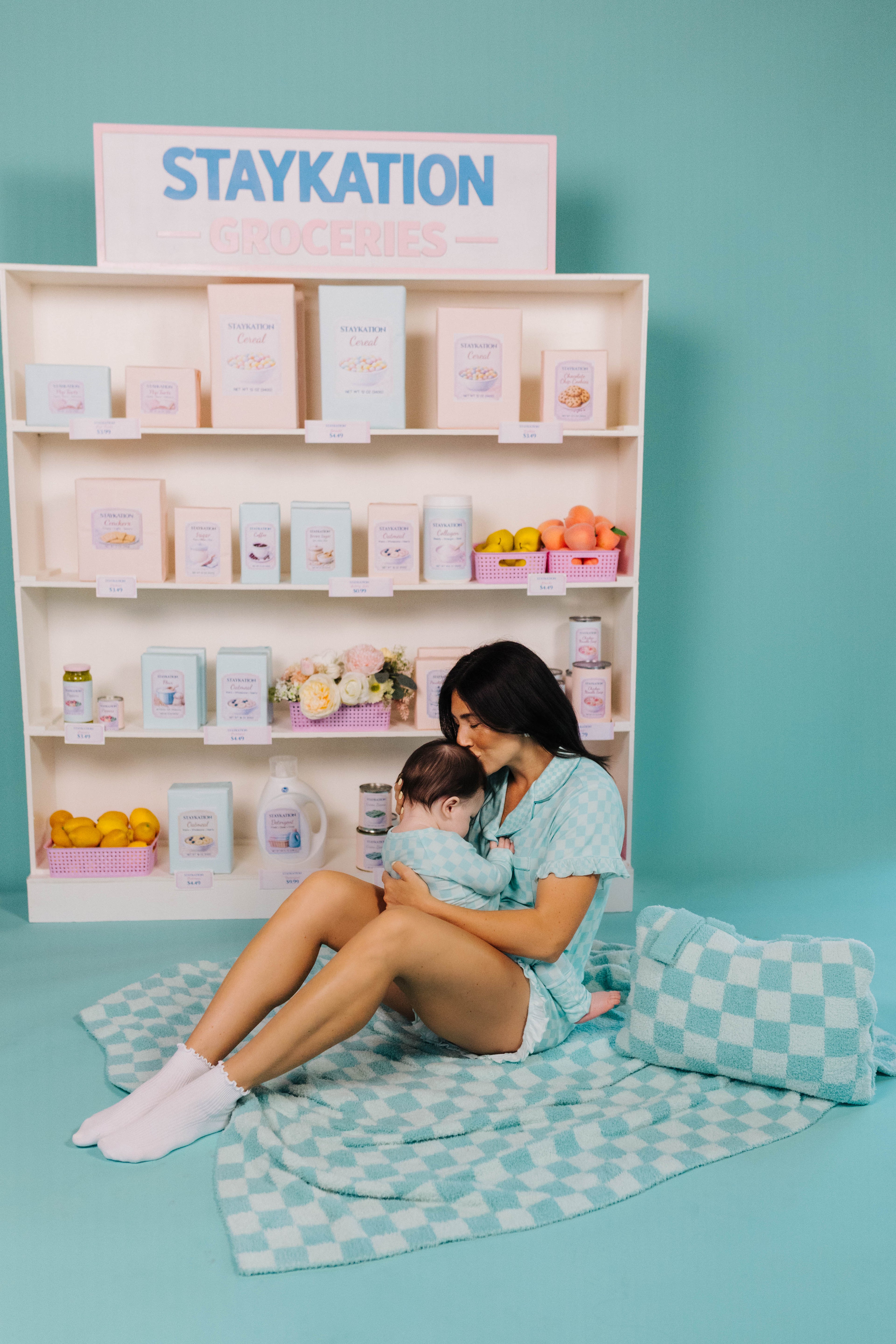 Woman and child sitting on a checkered blanket in front of a display with 'Staykation' branding.