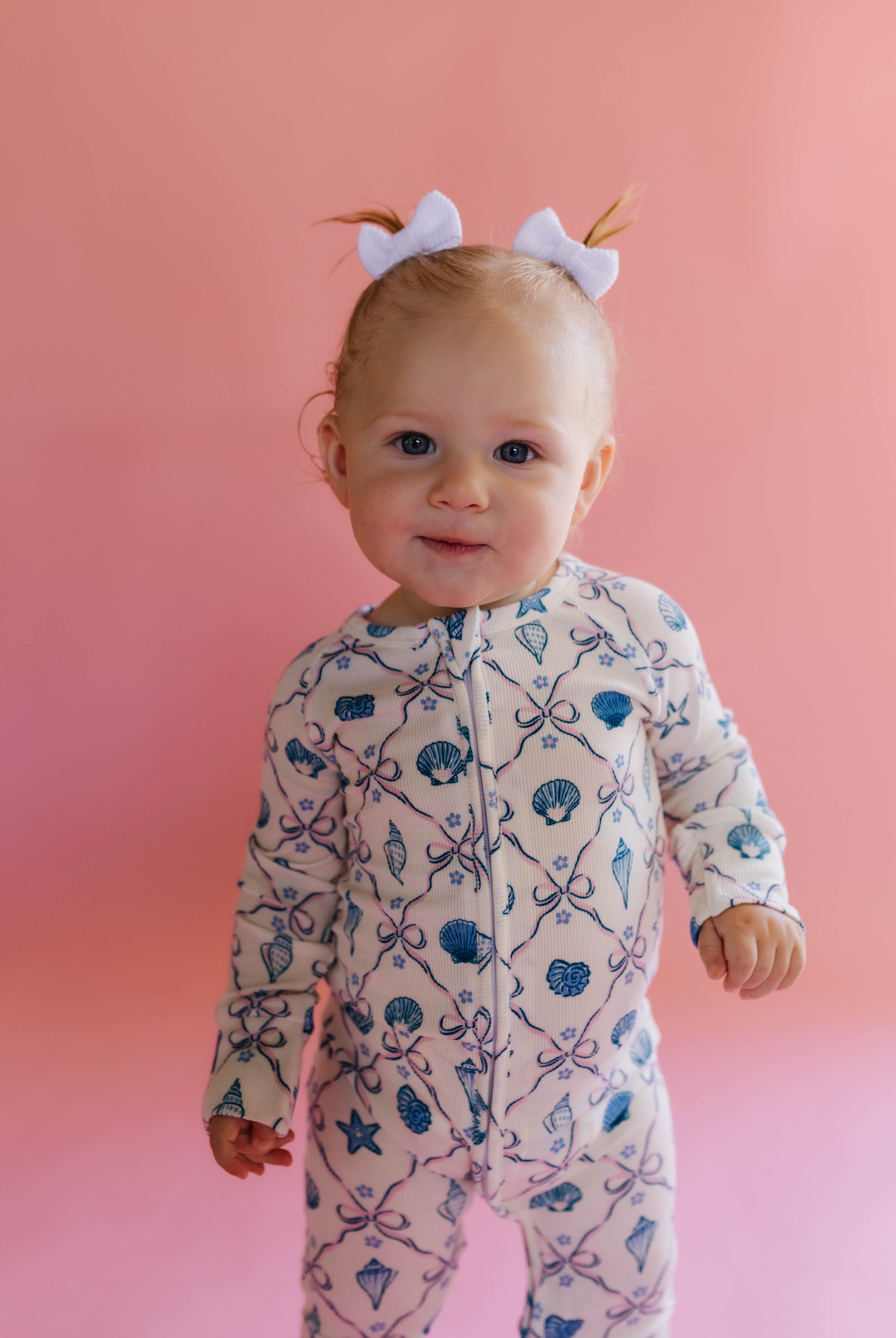 Baby wearing a patterned shell onesie against a pink background