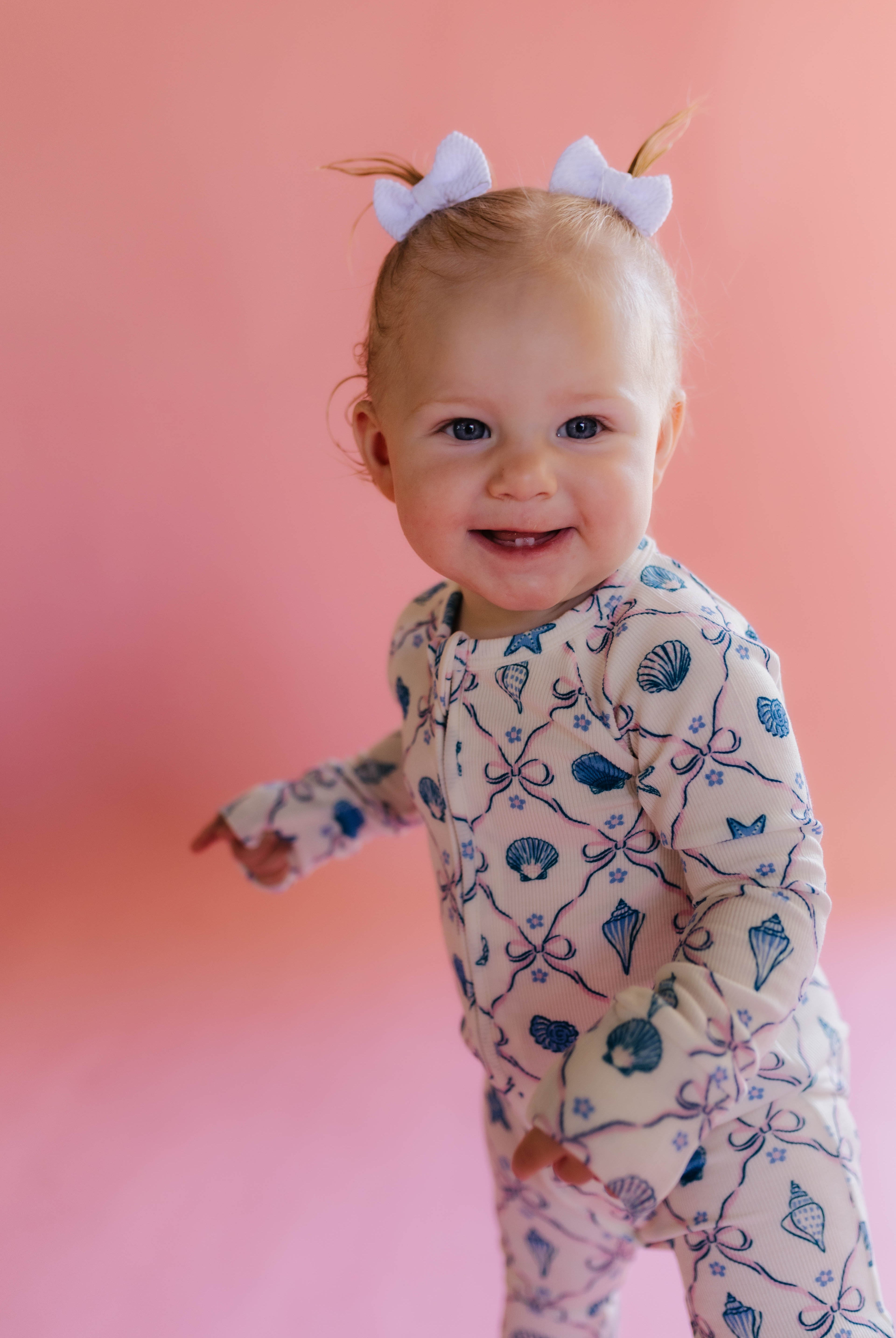 Baby wearing a patterned shell onesie on a pink background smiling