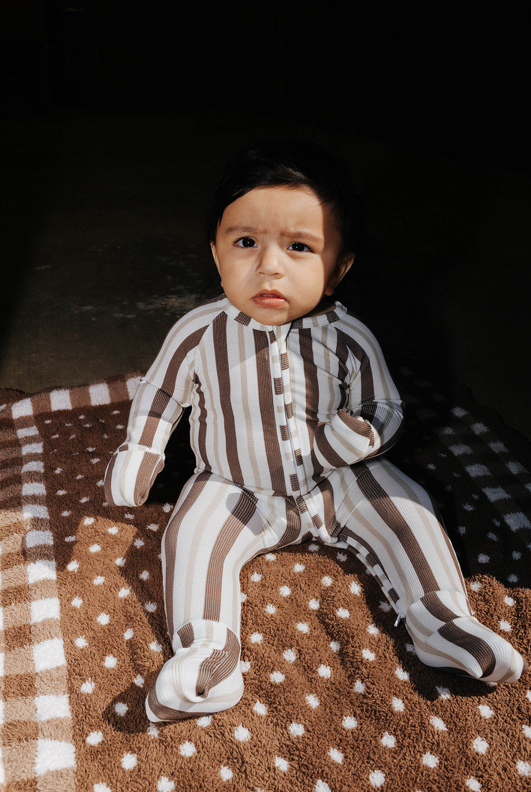 Baby wearing the brown and cream striped zip pajamas while seated on a brown blanket.