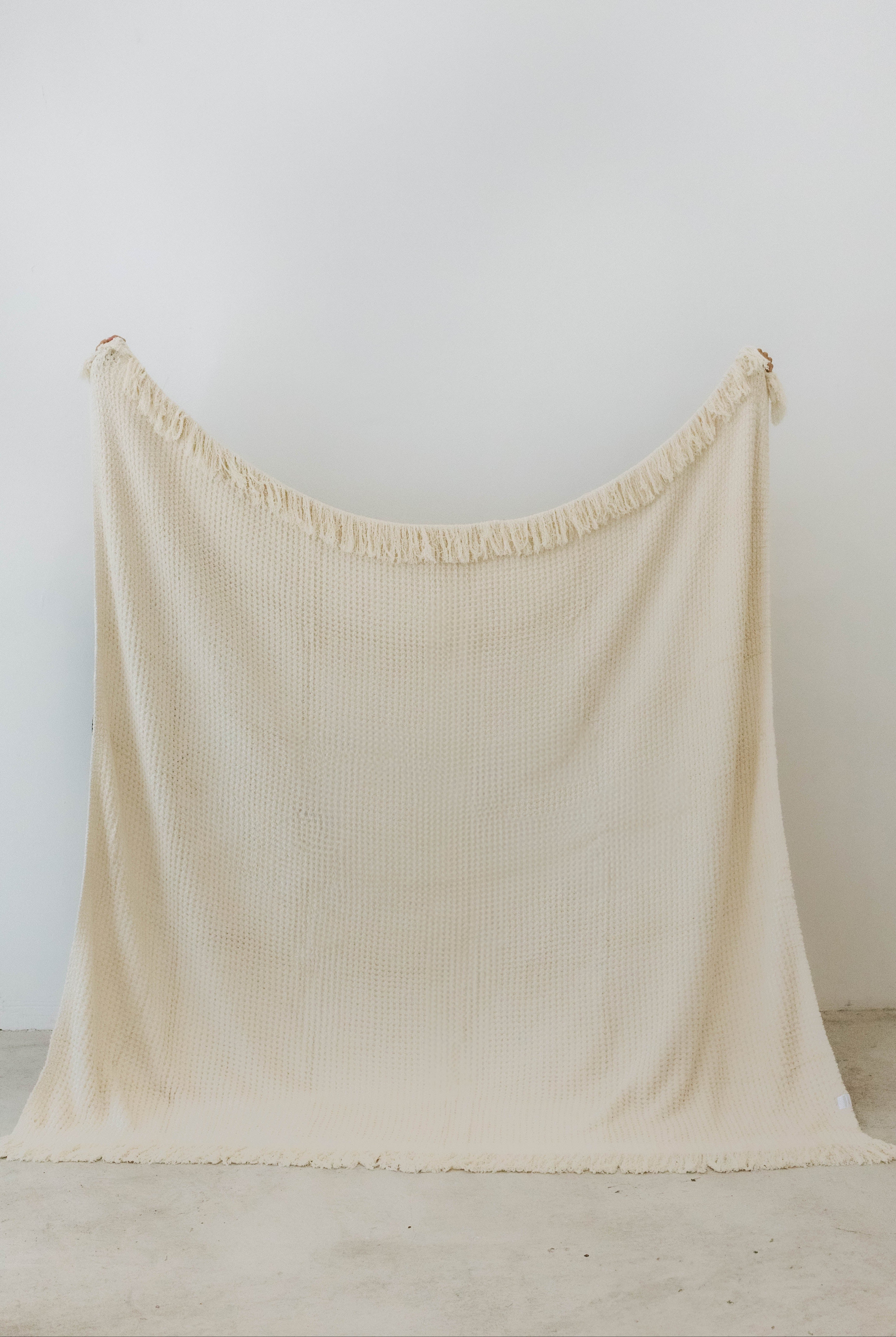 holding up cream waffle fringe blanket showing the size of the blanket