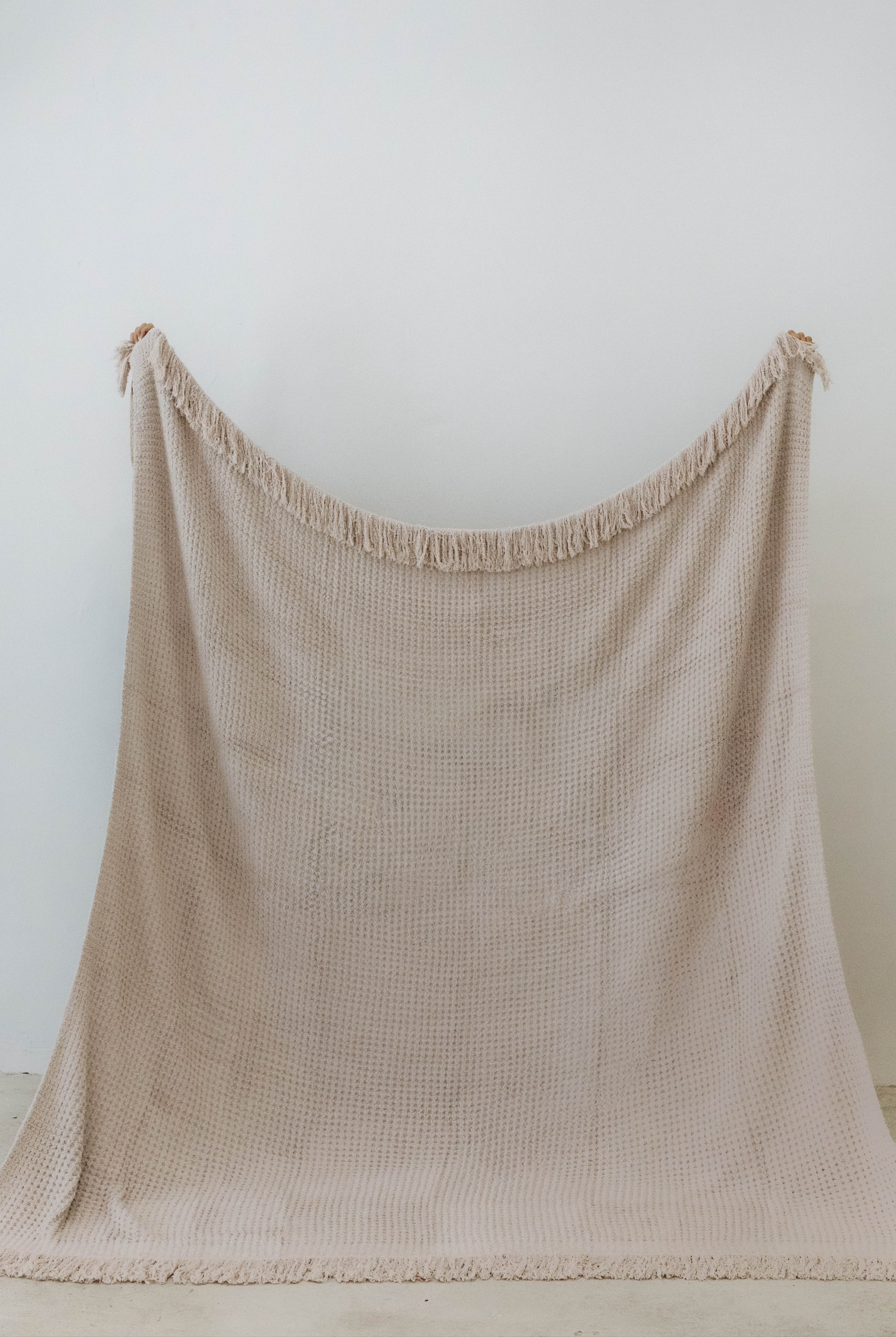 holding up the sand waffle fringe blanket showing the size of it