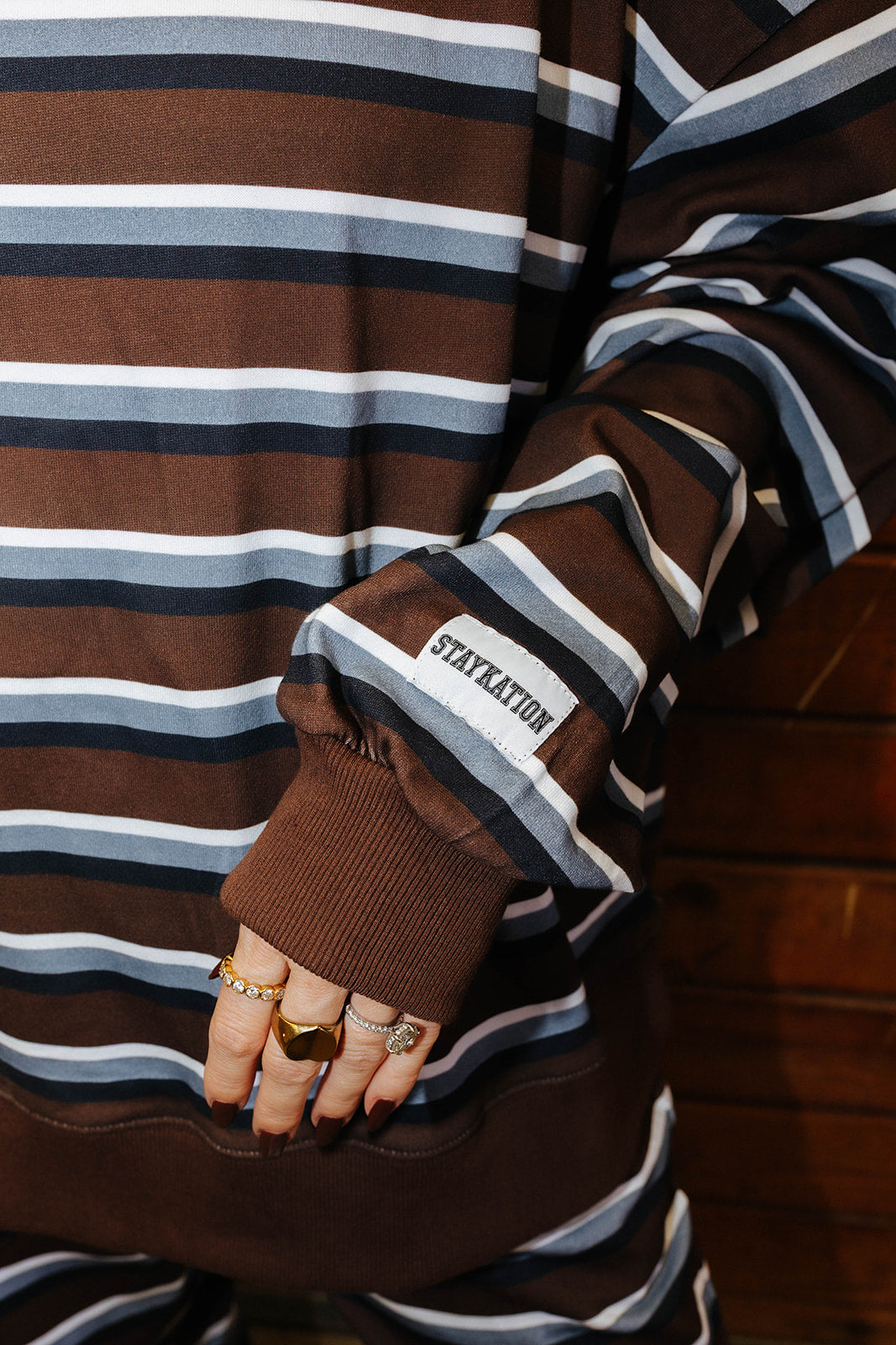 Close view of the striped sweatshirt cuff, brown ribbed trim, and Staykation label.