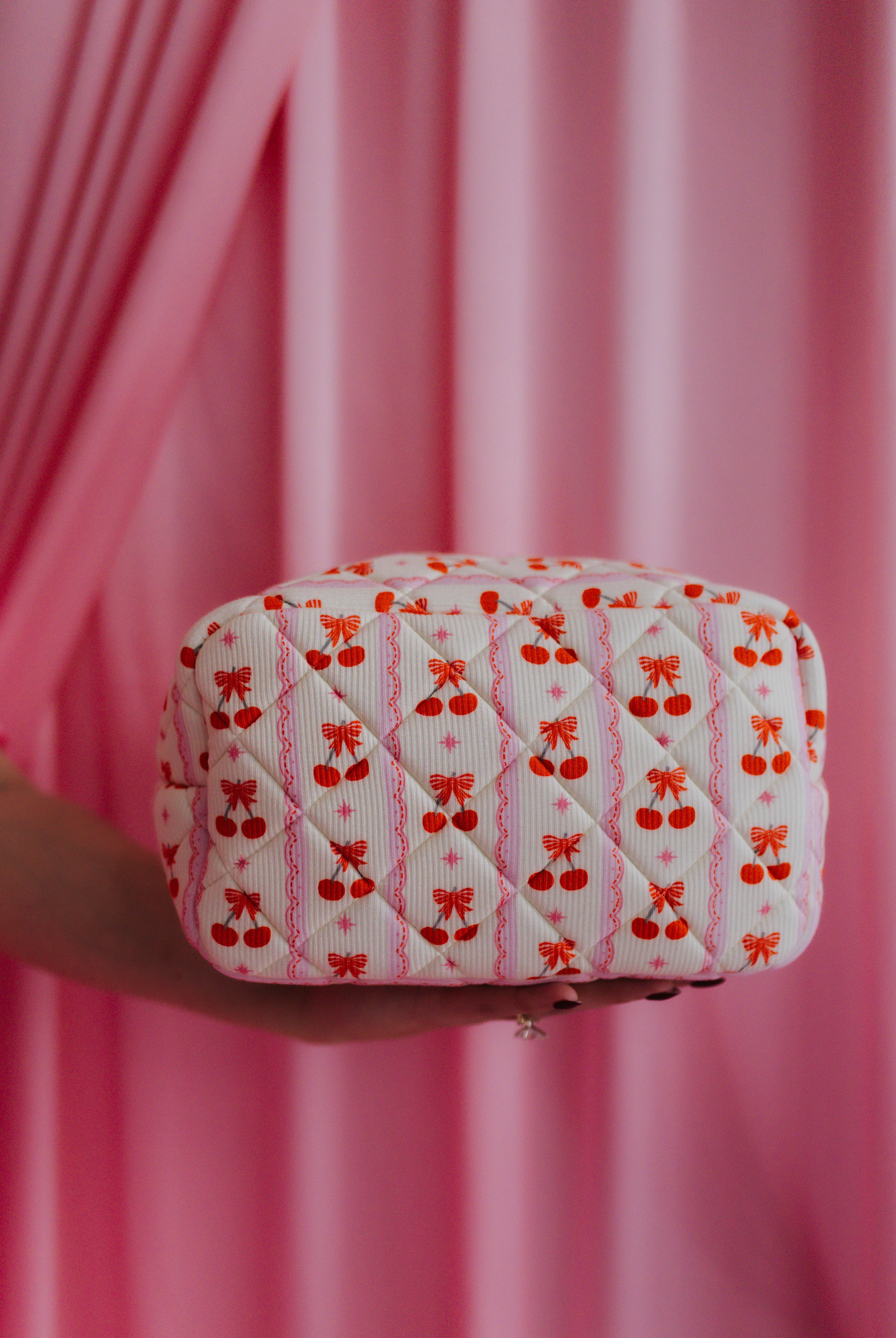 Quilted fabric pouch with red bow and cherrt pattern held against a pink curtain