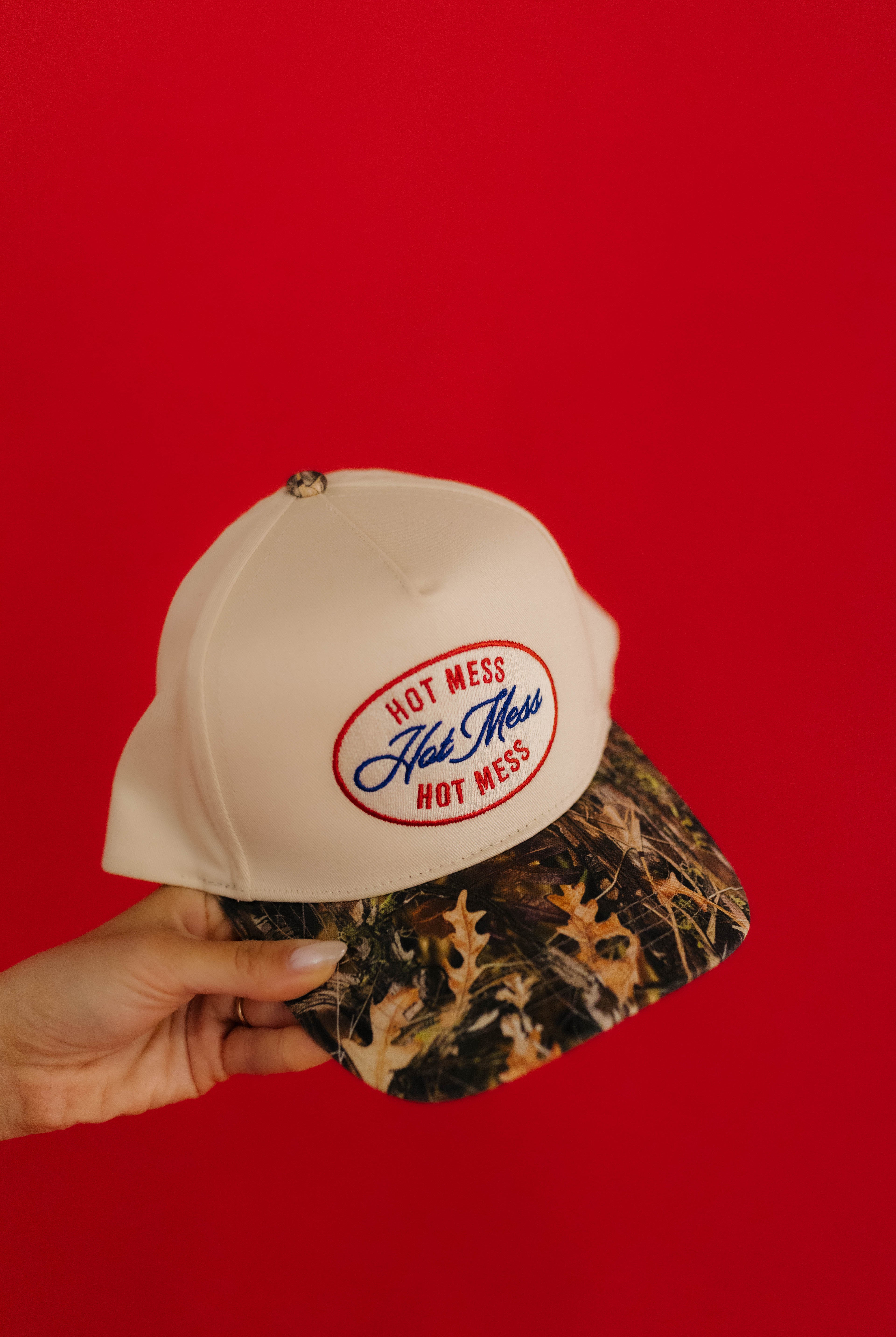 Cream cap with 'Hot Mess' logo held against a red background