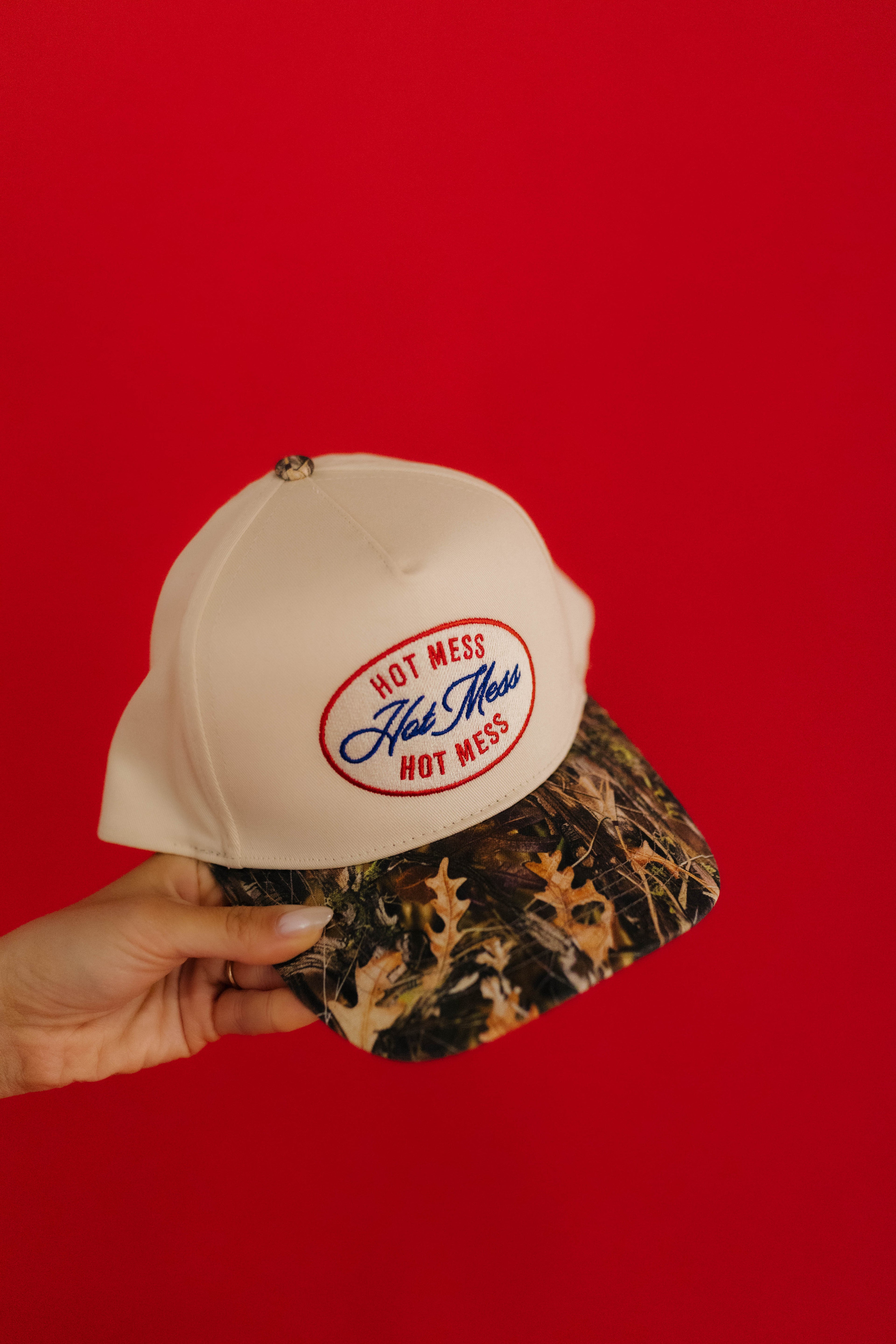 Cream cap with 'Hot Mess' logo held against a red background