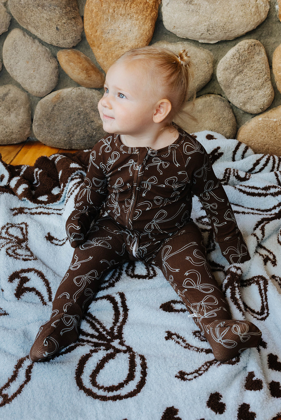 Side view of a baby wearing brown bow print zip pajamas on a matching bow quillow.