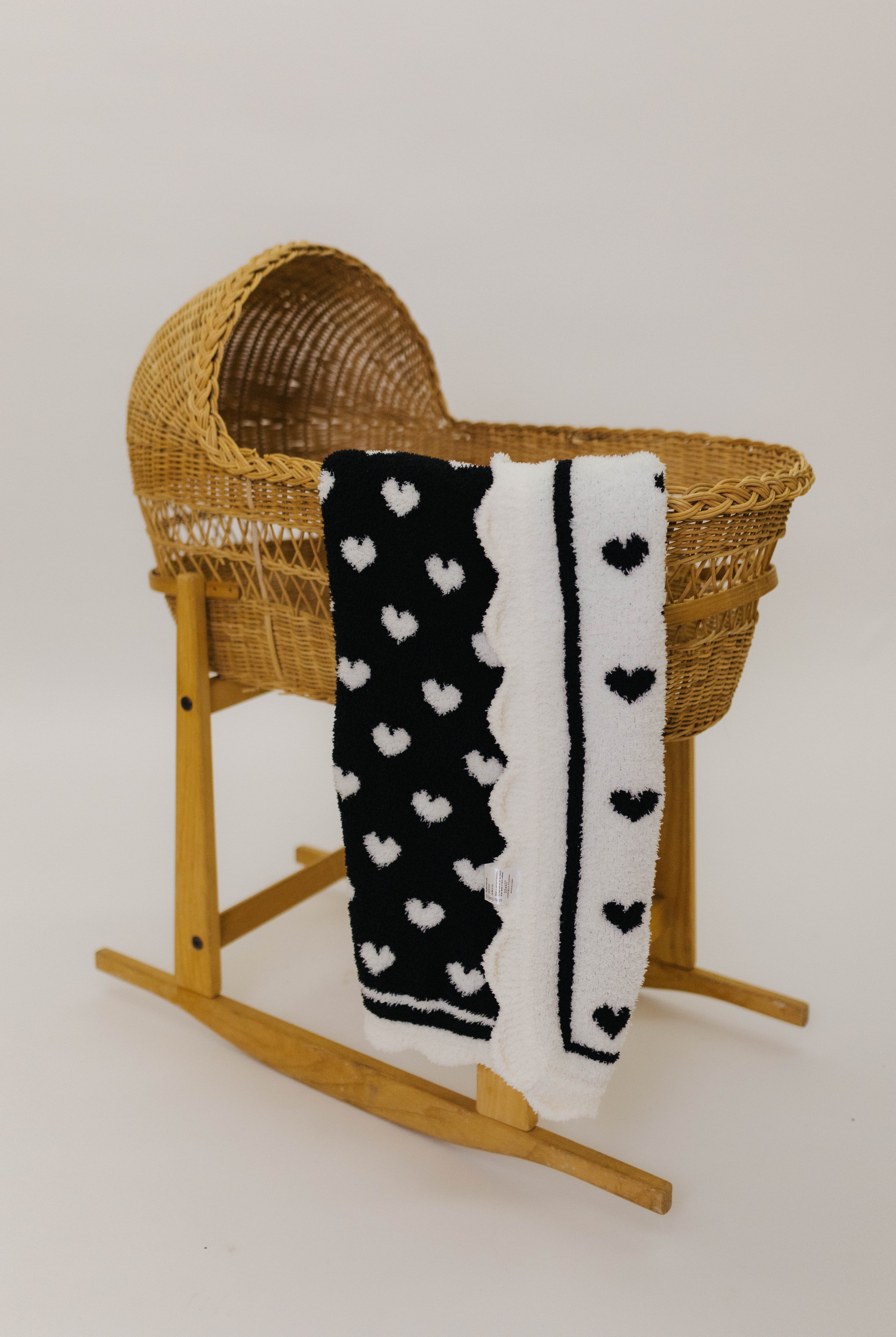 Wicker baby crib with a black and white heart-patterned blanket on a plain background
