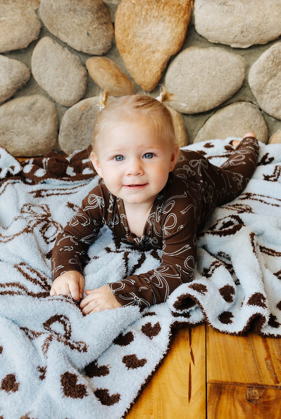 Baby in brown bow print zip pajamas on a blanket.