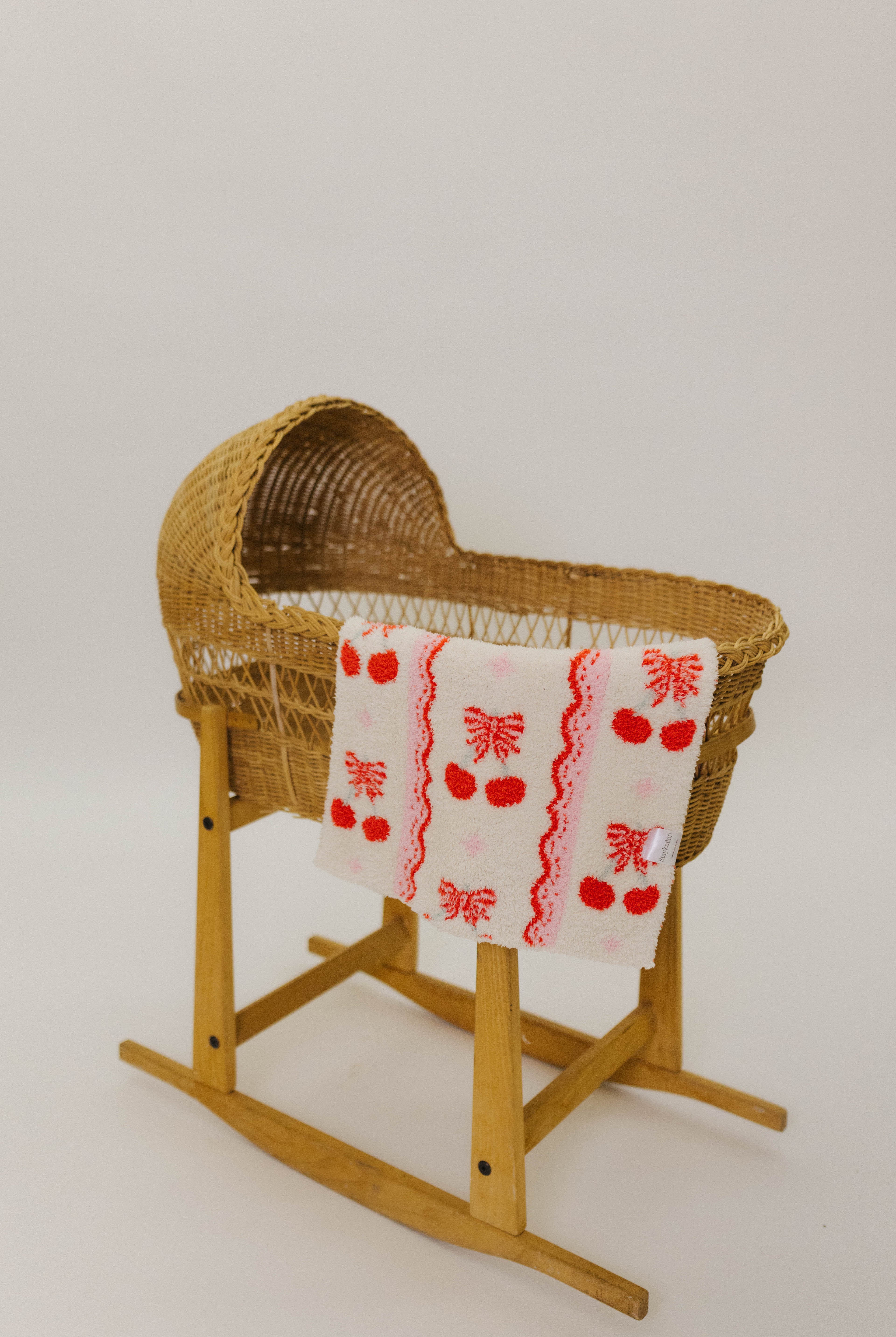 Wicker baby bassinet with a red and white patterned cherry blanket on a white background