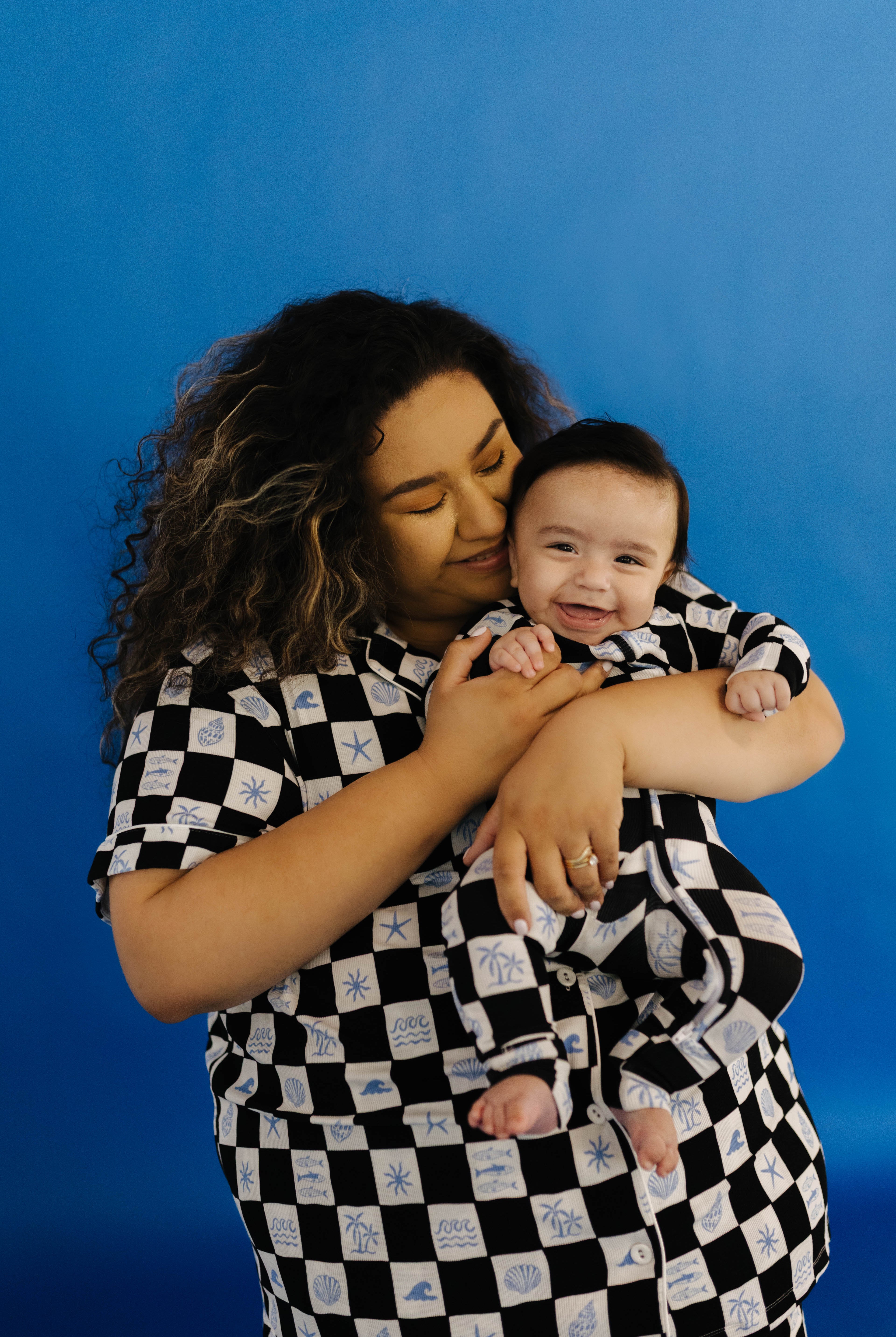 Woman and baby in matching black and white checkered pjs against a blue background