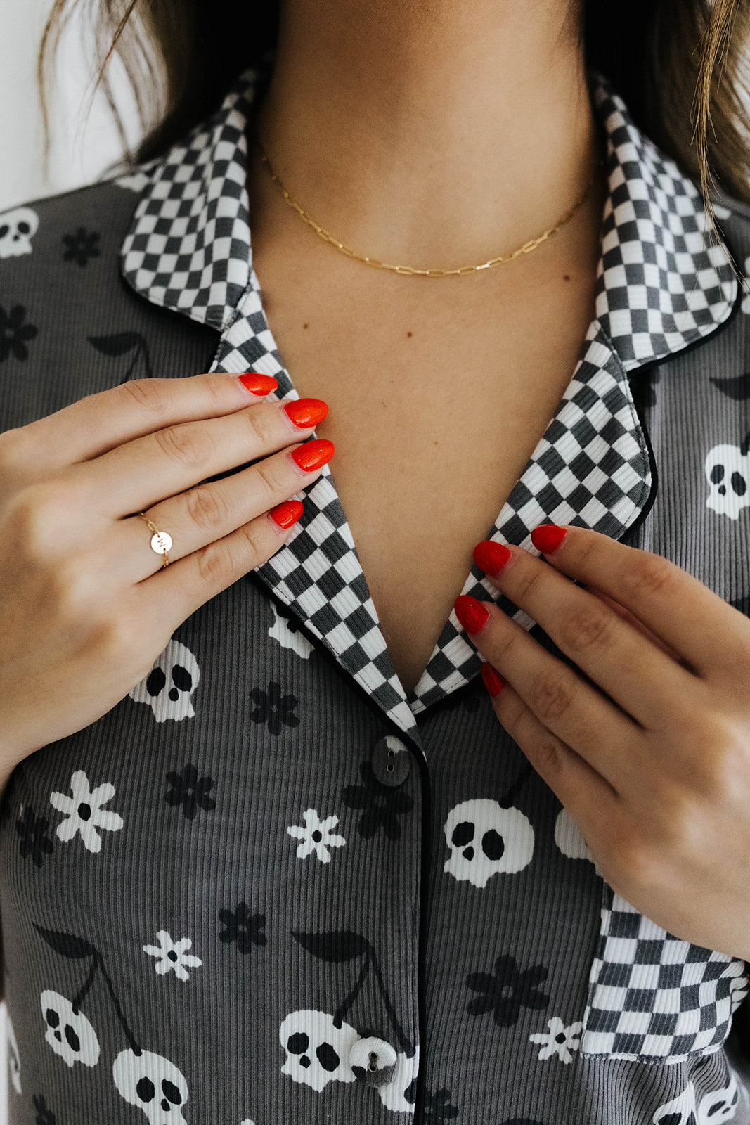 model with red nails showing the collar of the skeleton pajamas. The collar is grey and white checkered print