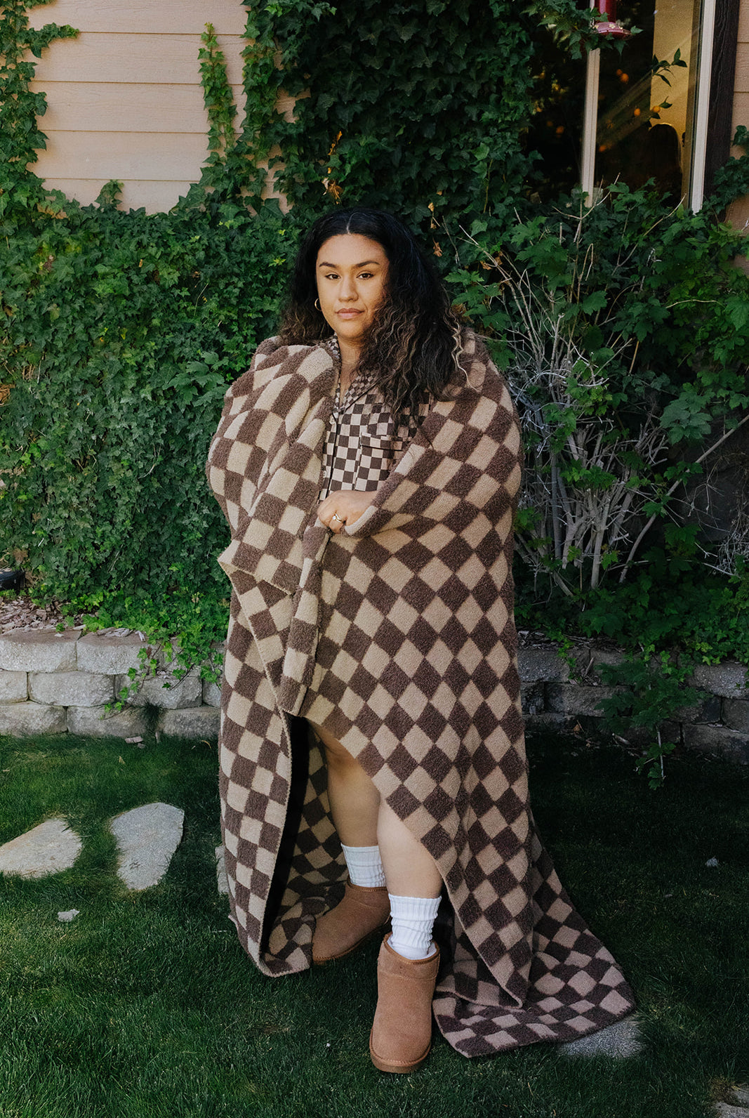Model holding the tonal brown check blanket open outdoors to show its full size.