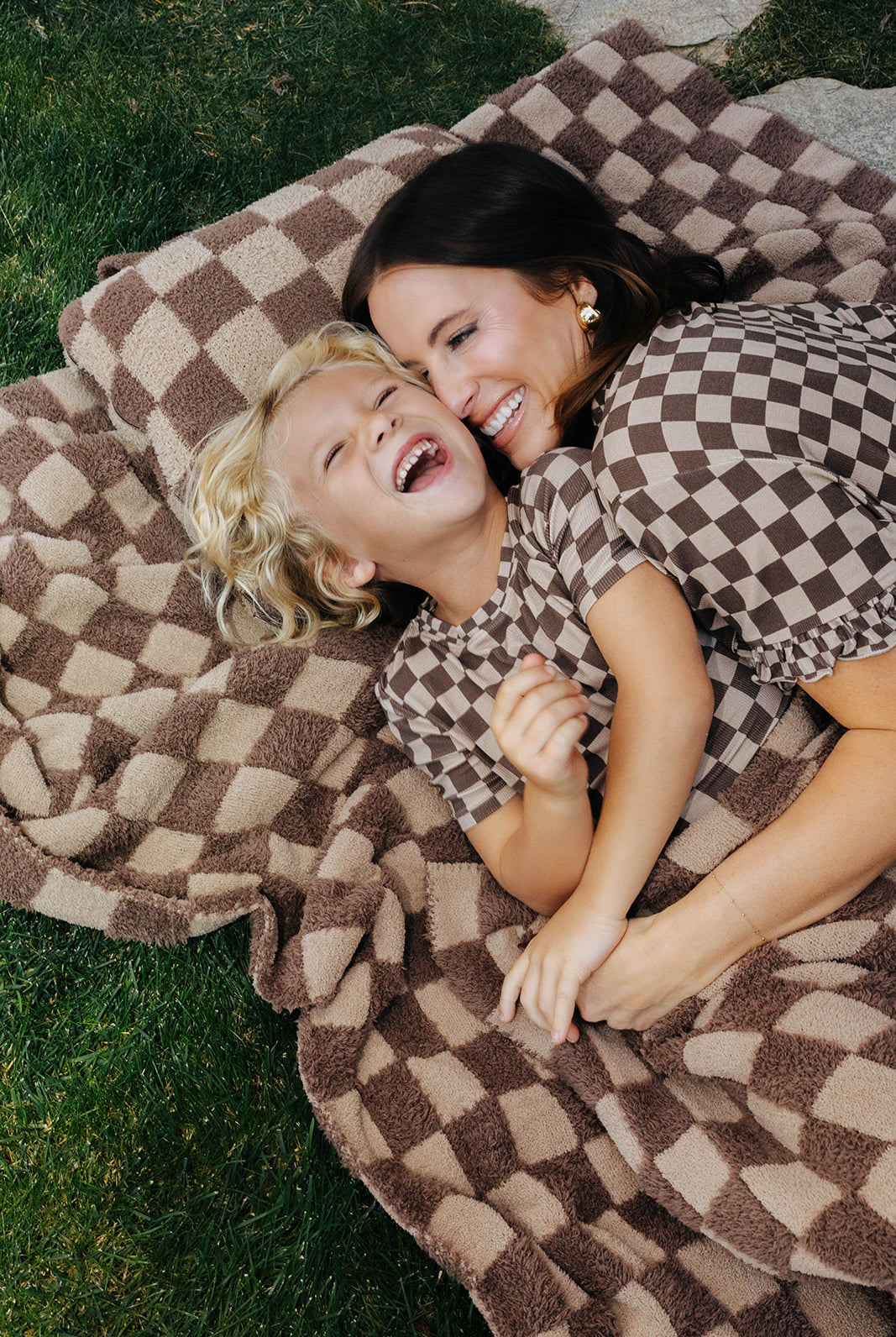 Adult and children in matching brown check pajamas lying on a tonal brown check blanket.