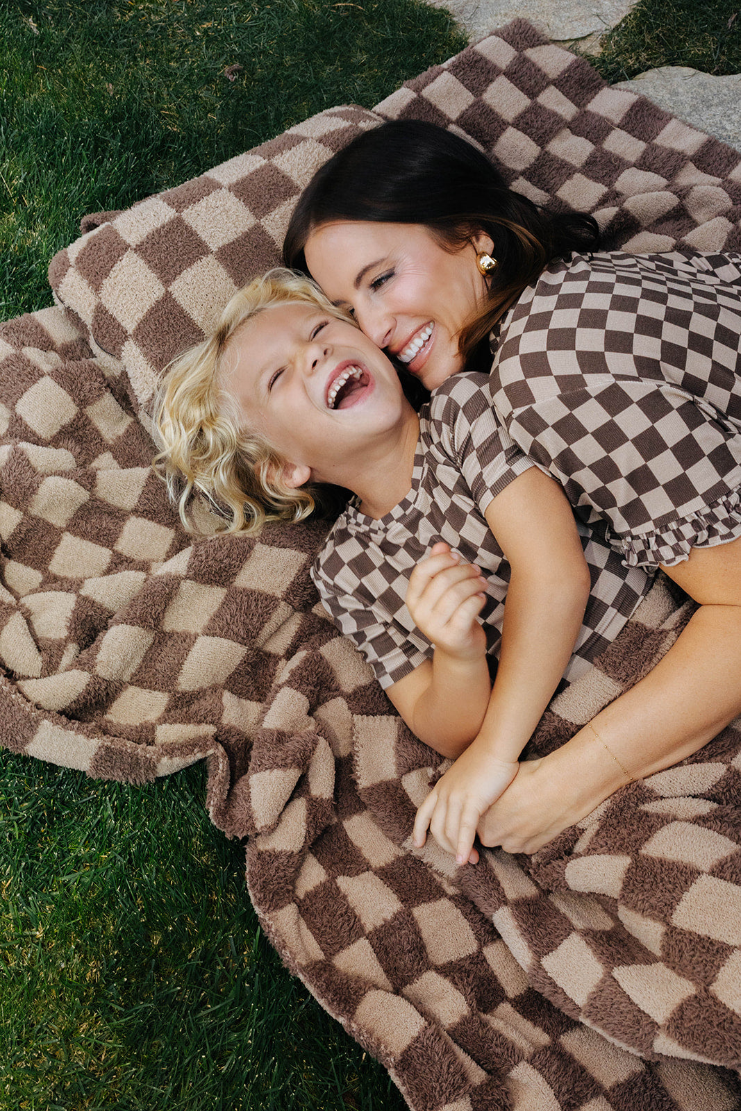 Adult and children in matching brown check pajamas lying on a tonal brown check blanket.