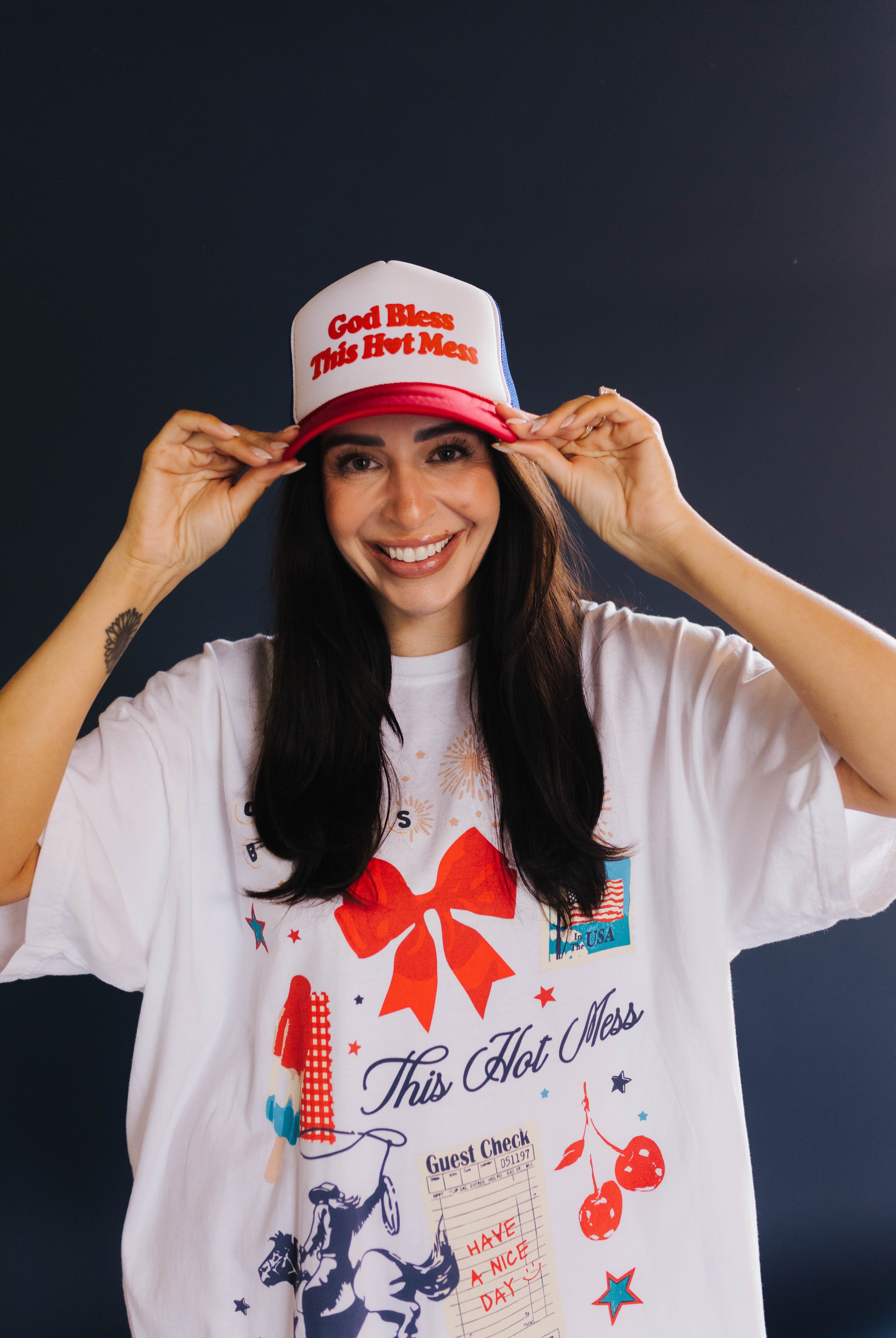 person smiling showing the front of the hat that says god bless this hot mess
