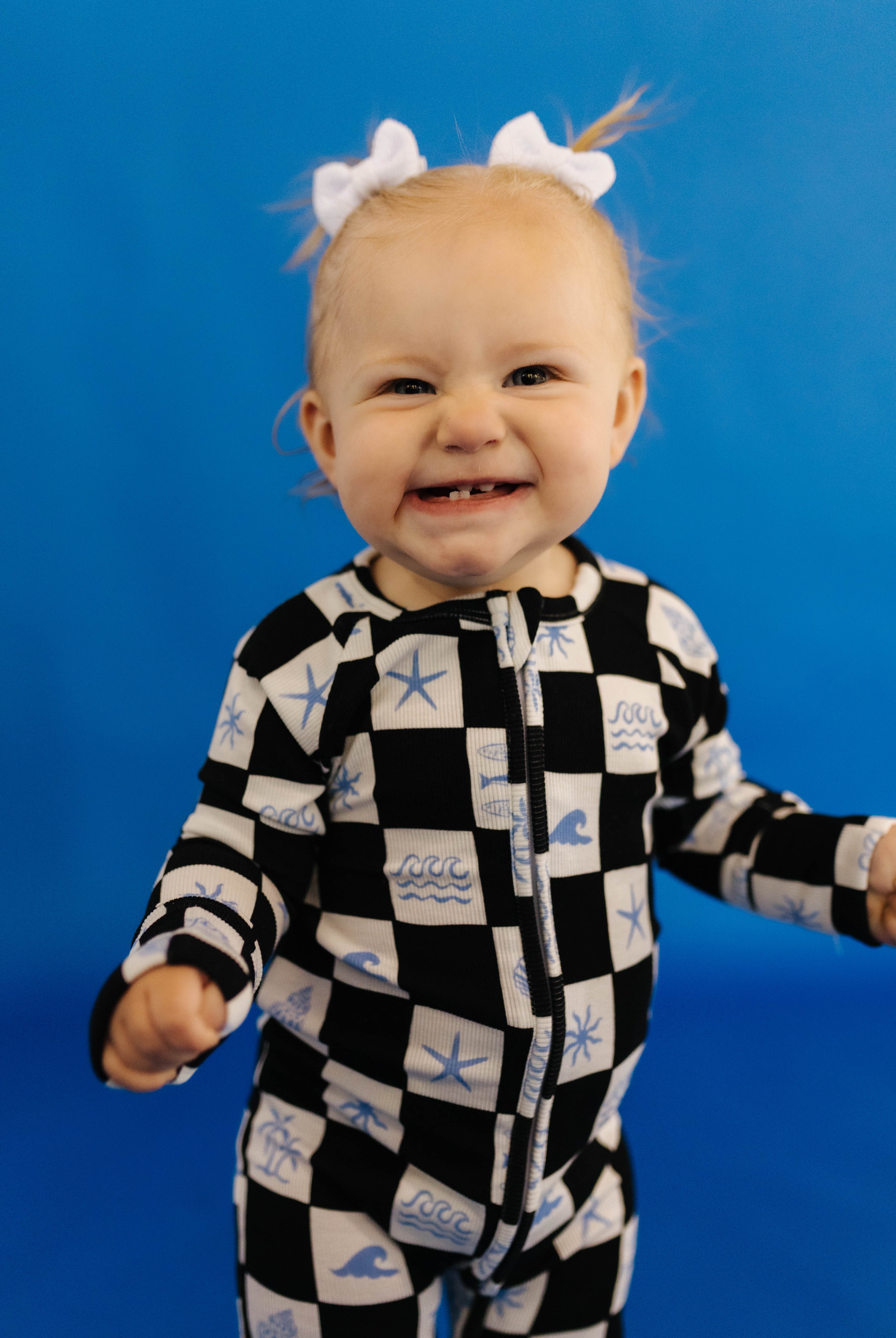 Child wearing a black and white checkered onesie with blue sea-themed designs against a blue background