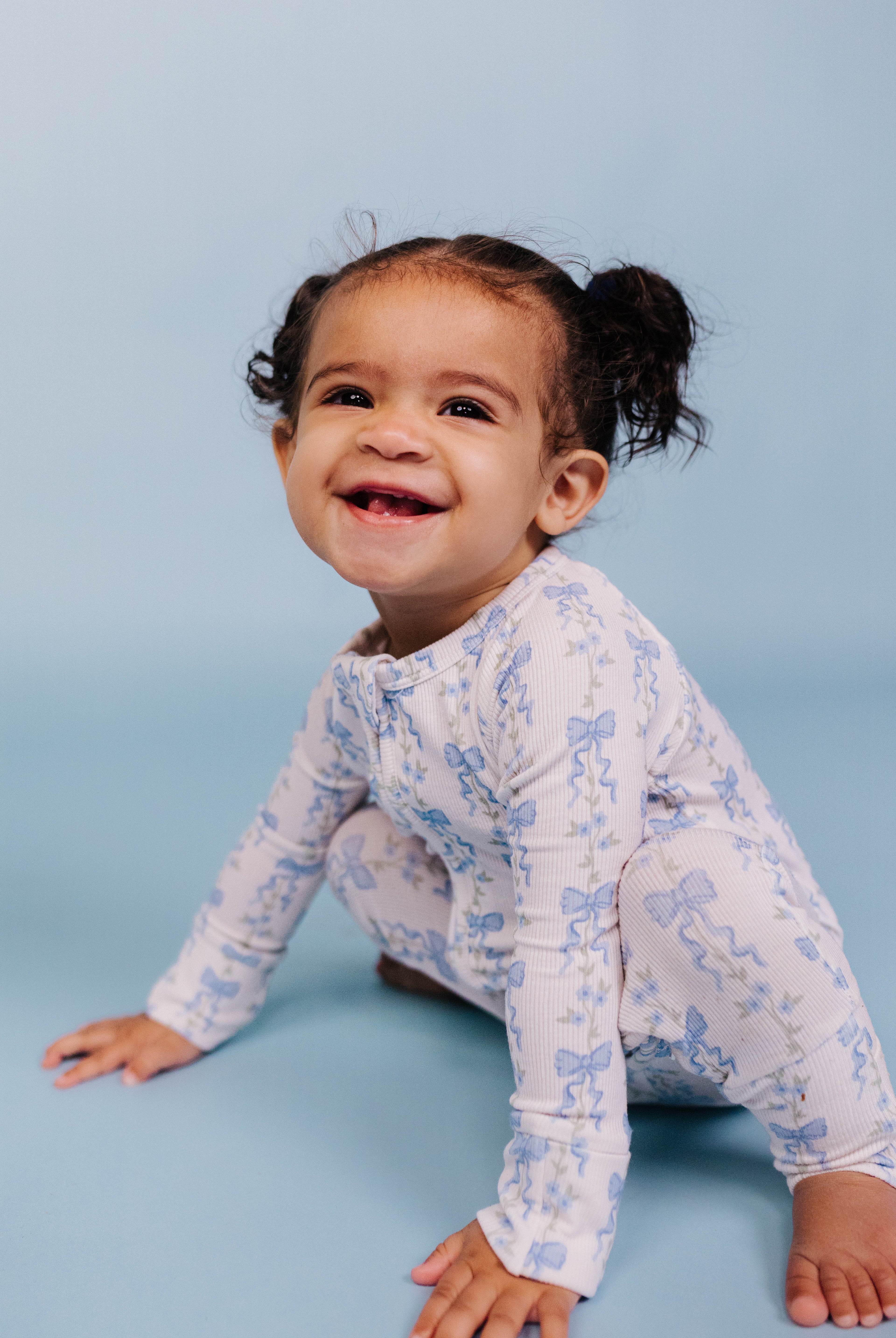 Child wearing a white long-sleeve baby romper with blue patterns on a light blue background