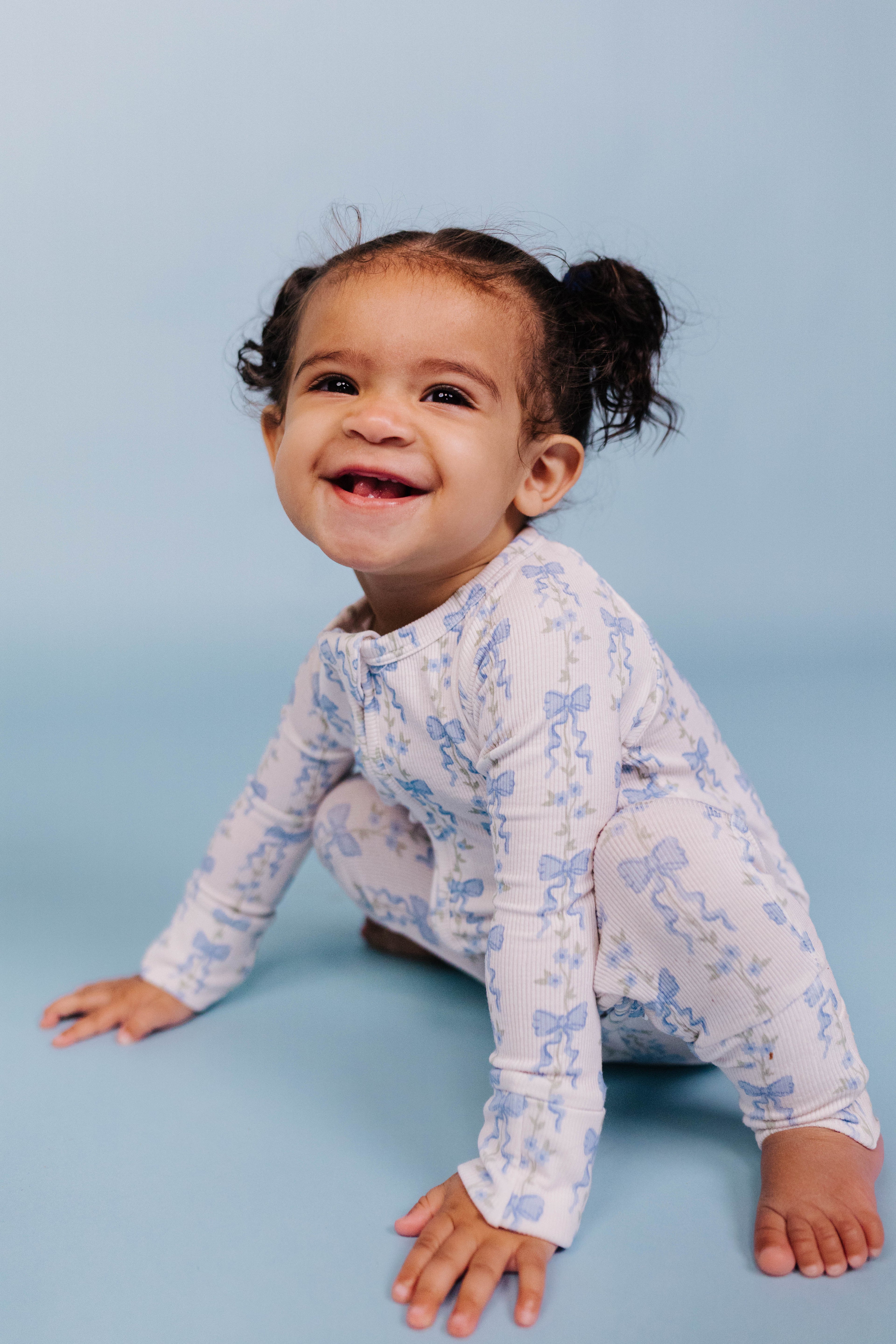 Child wearing a white long-sleeve baby romper with blue patterns on a light blue background
