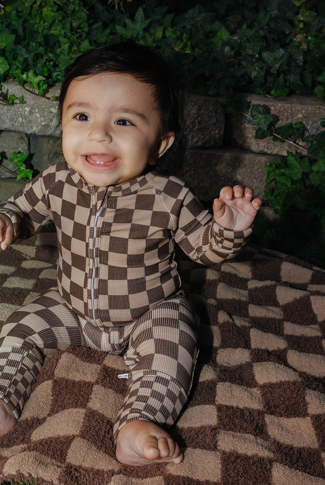 Baby wearing the brown check zip pajamas while seated on a blanket.