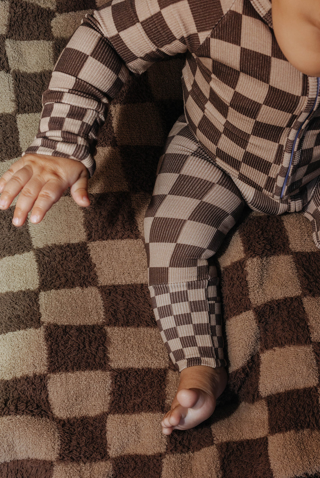 Close view of a baby wearing brown check zip pajamas on a tonal brown check kid blanket.