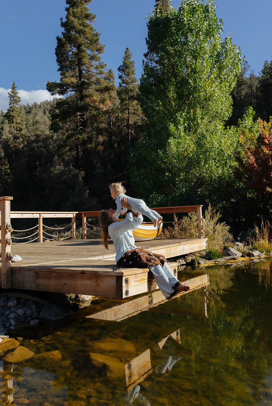 Adult sitting on a lakeside dock holding a baby in pale blue polka dot zip pajamas.