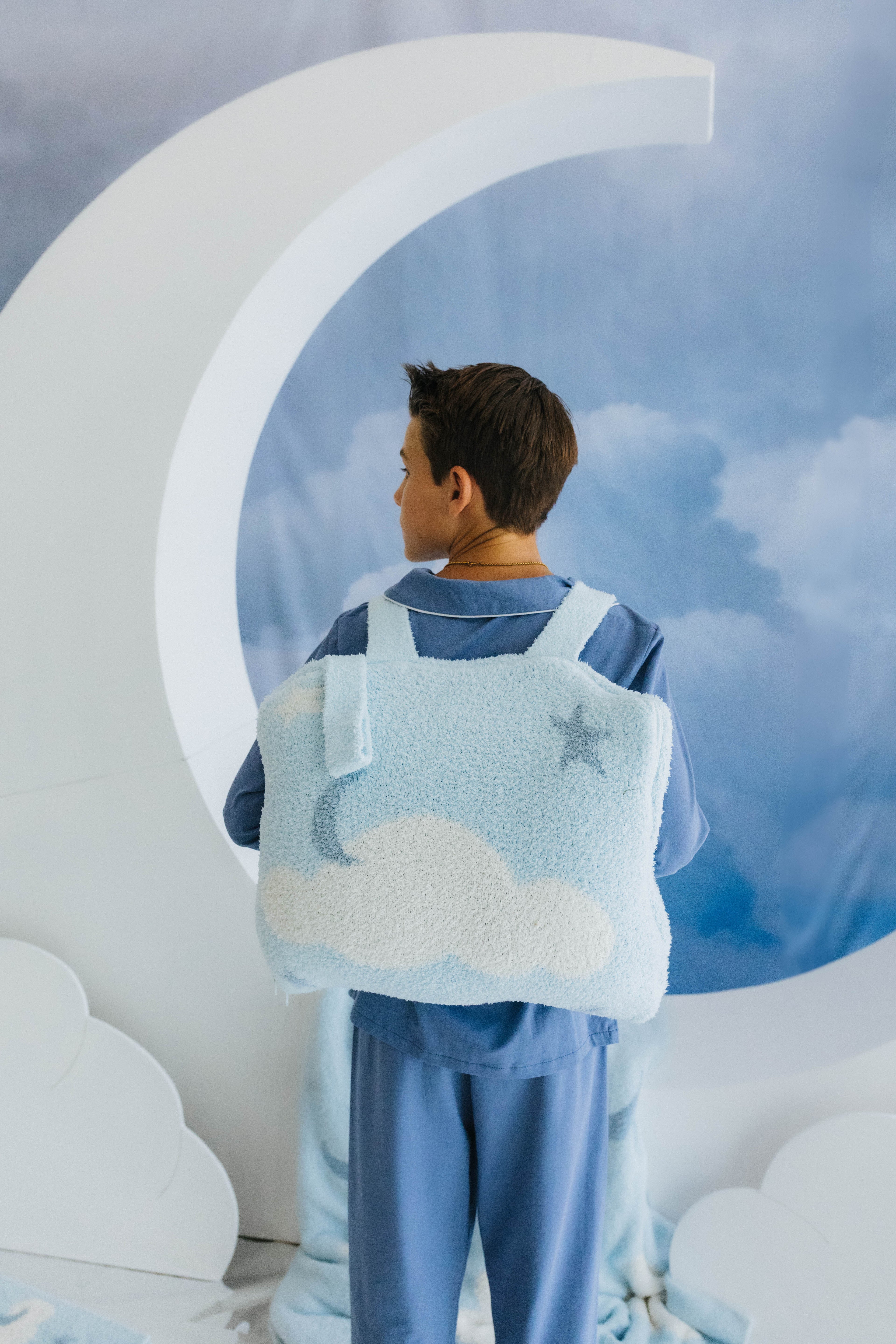 model wearing cloud backpack/wristlet quillow on back with cloud decorations in the background