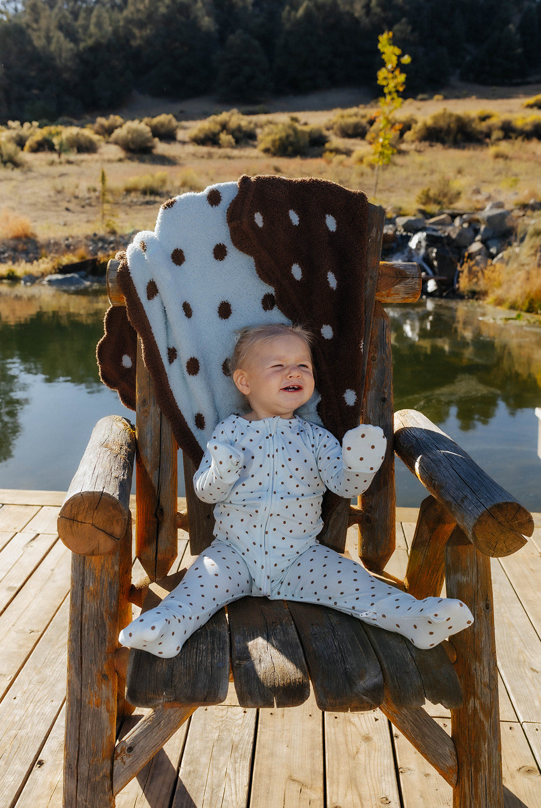 Full length front view of baby blue and brown polka dot zip pajamas, with hands and feet visible.