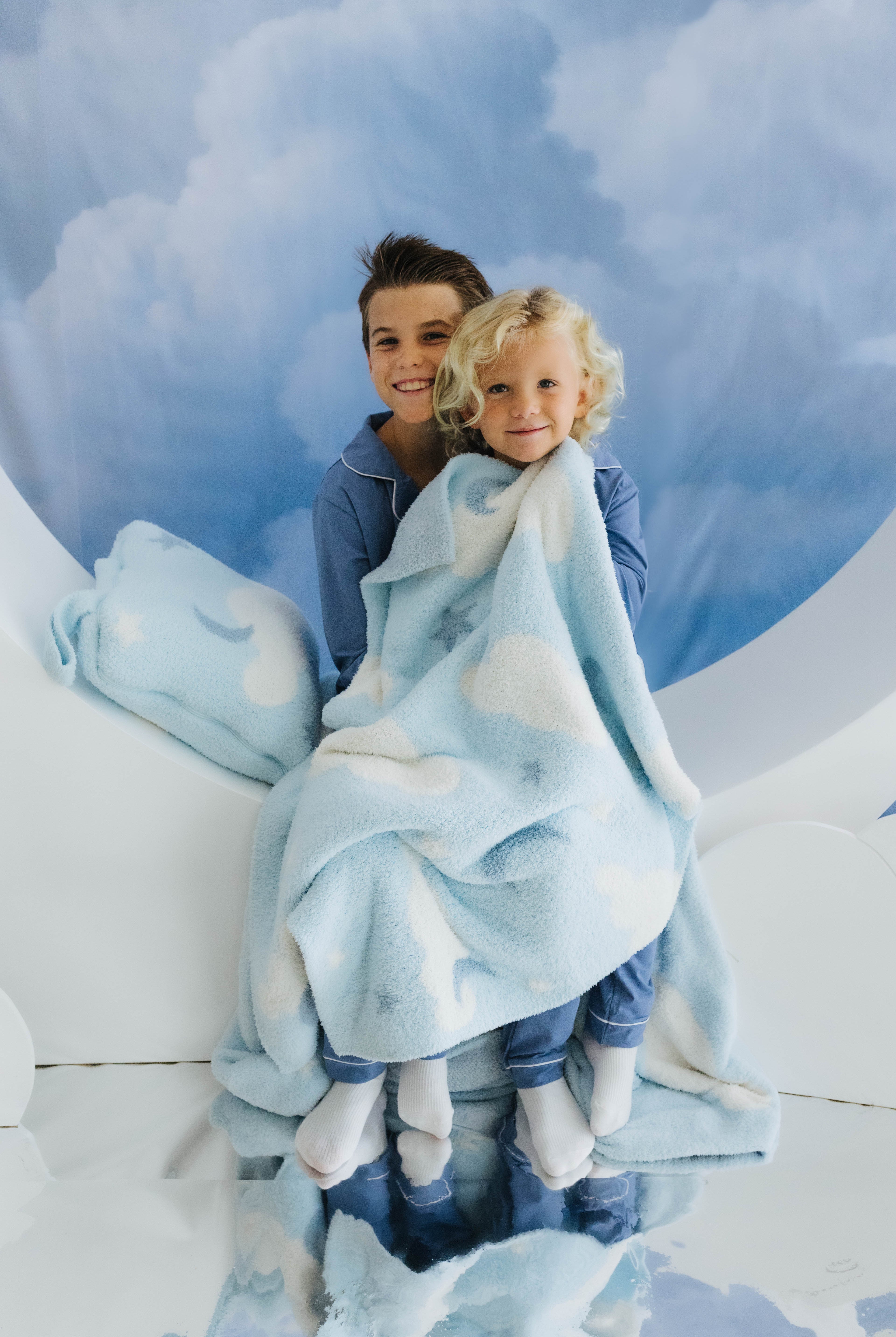 two kids sitting on moon decoration holding cloud baby blanket with cloud decorations in the back