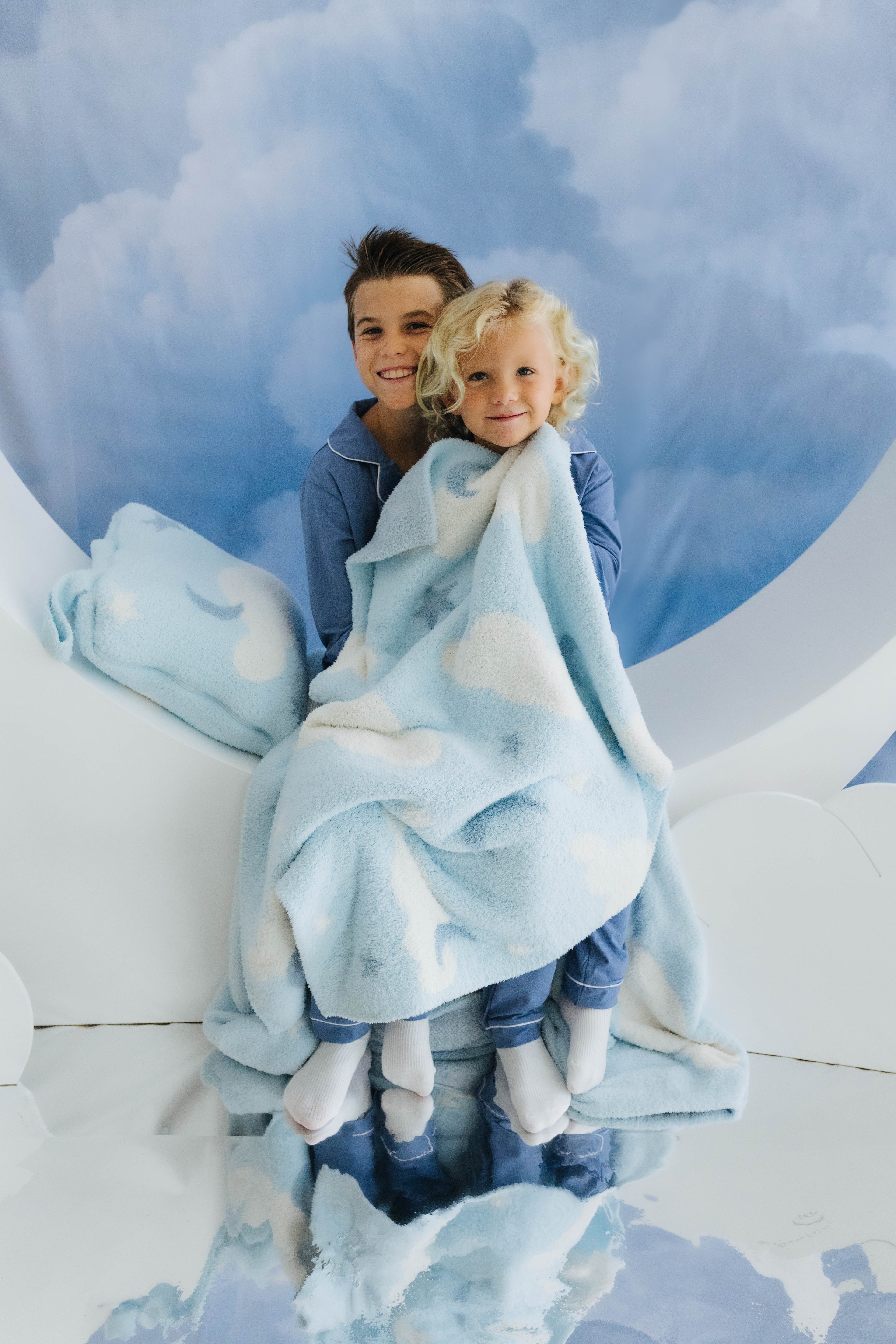 two kids sitting on moon decoration holding cloud baby blanket with cloud decorations in the back