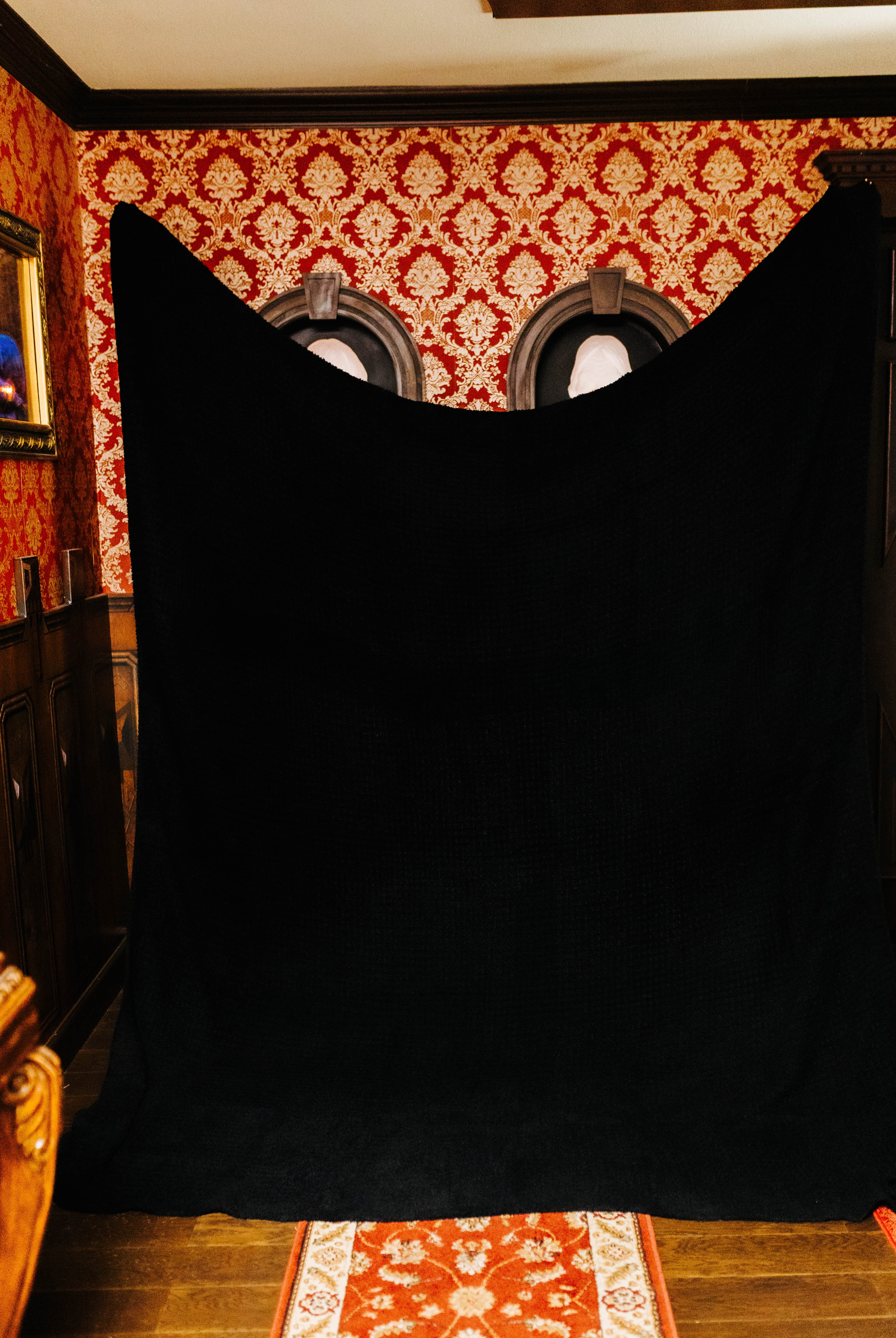 holding up the black non fringe blanket against a patterned wall