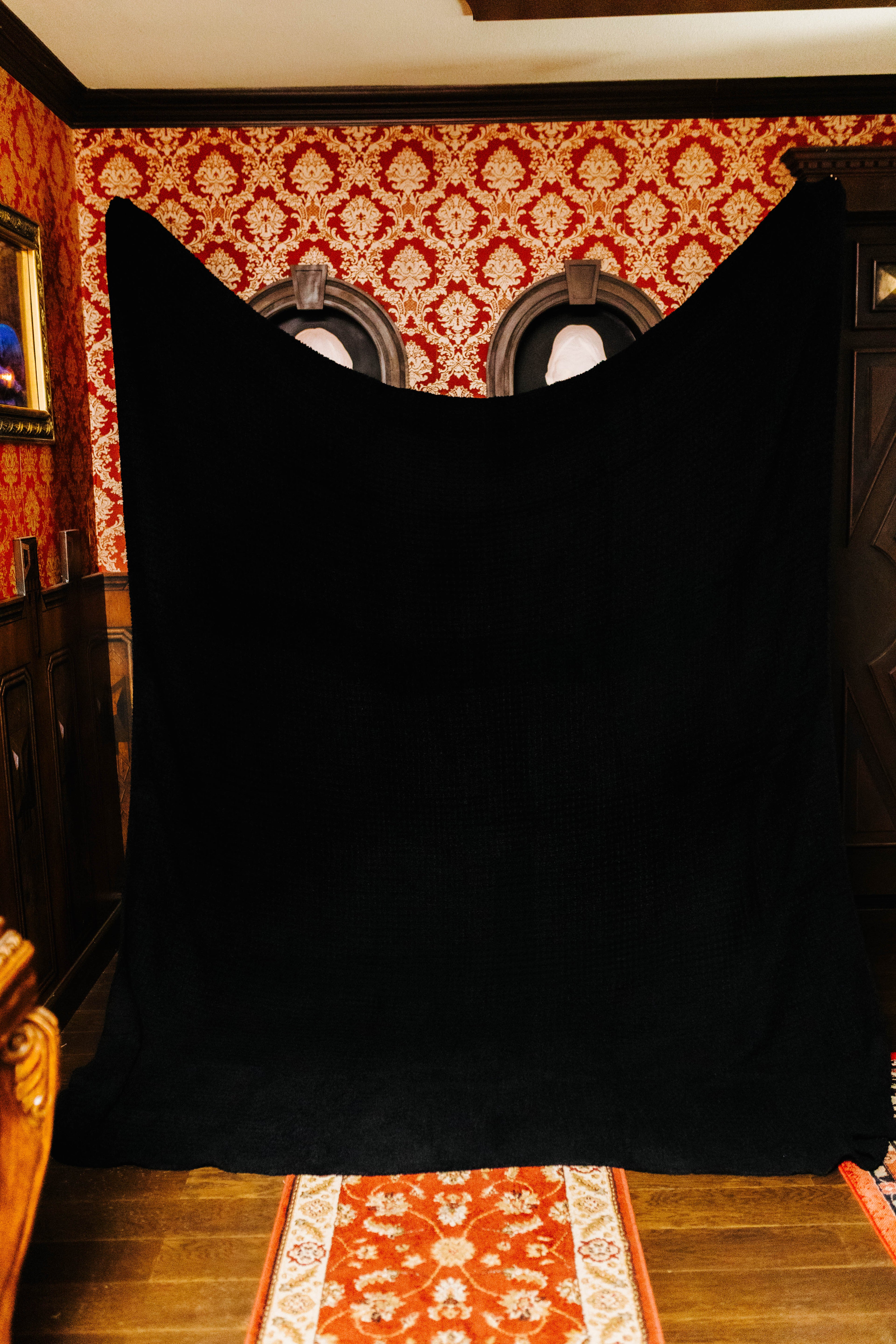 holding up the black non fringe blanket against a patterned wall