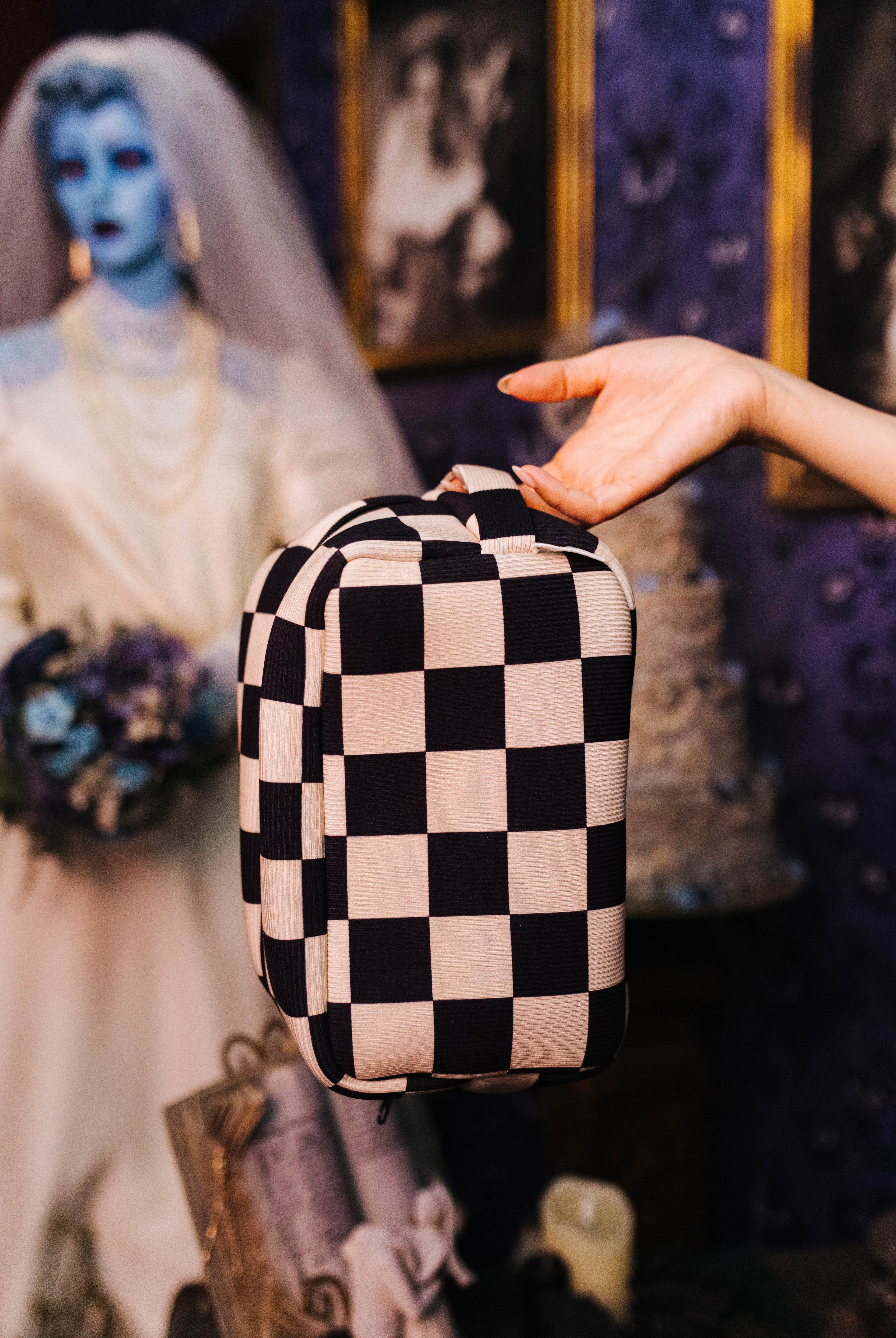 Sand and black check cosmetic bag held in front by its top handle
