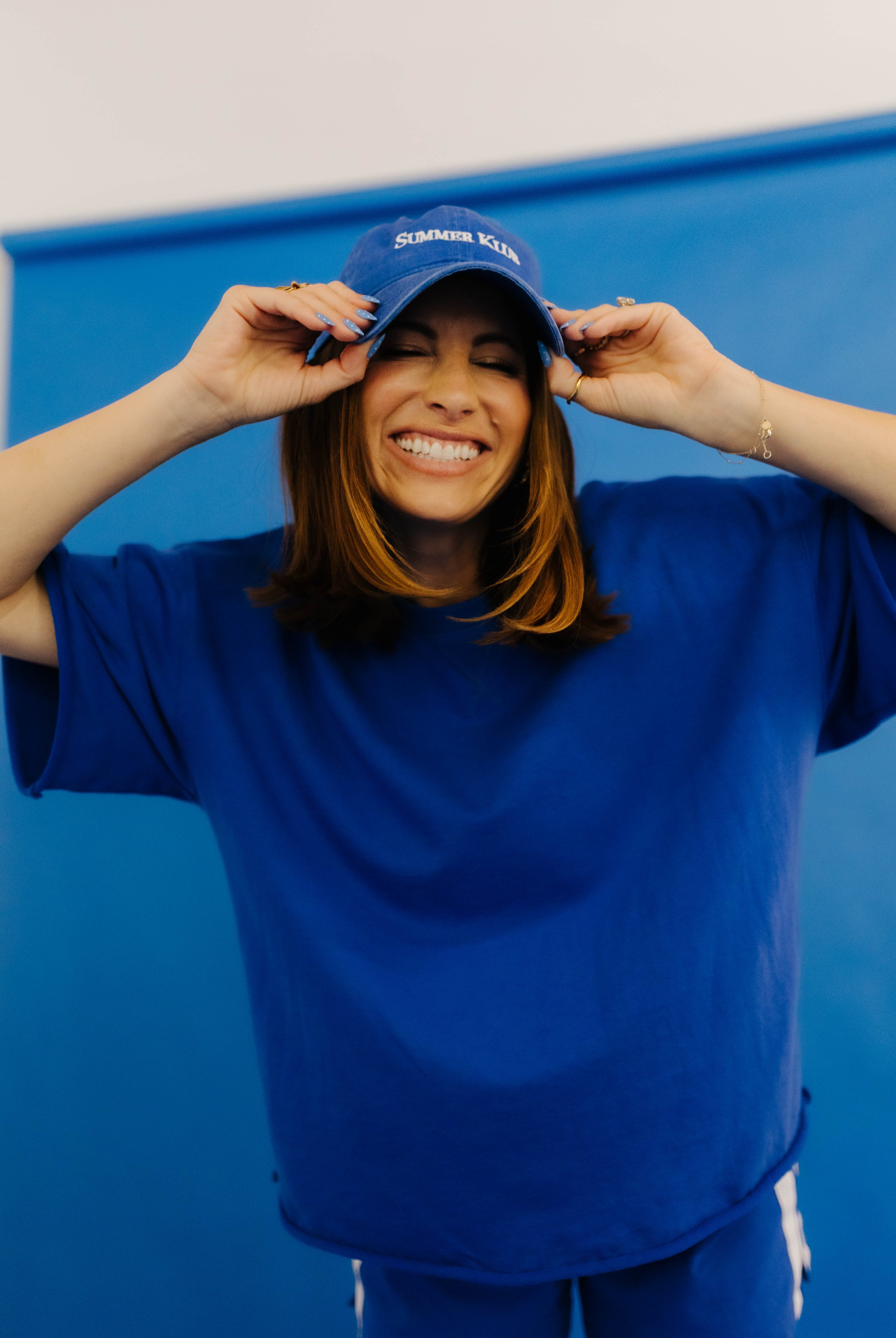 Person wearing a blue shirt and shorts with a blue cap, standing against a blue background