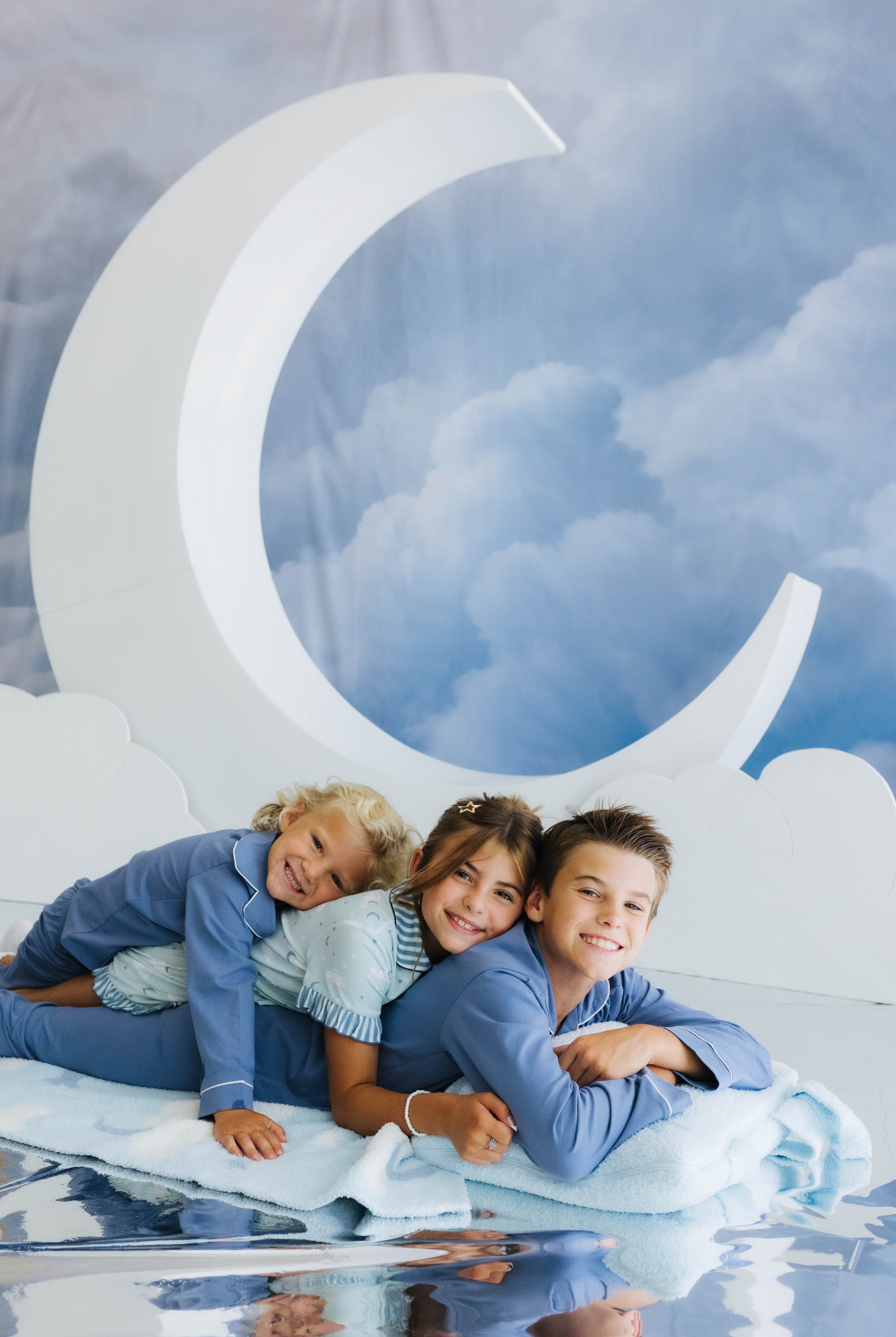 kids piled on top of one another smiling with cloud backpack/wristlet quillow and cloud and moon decorations in the back