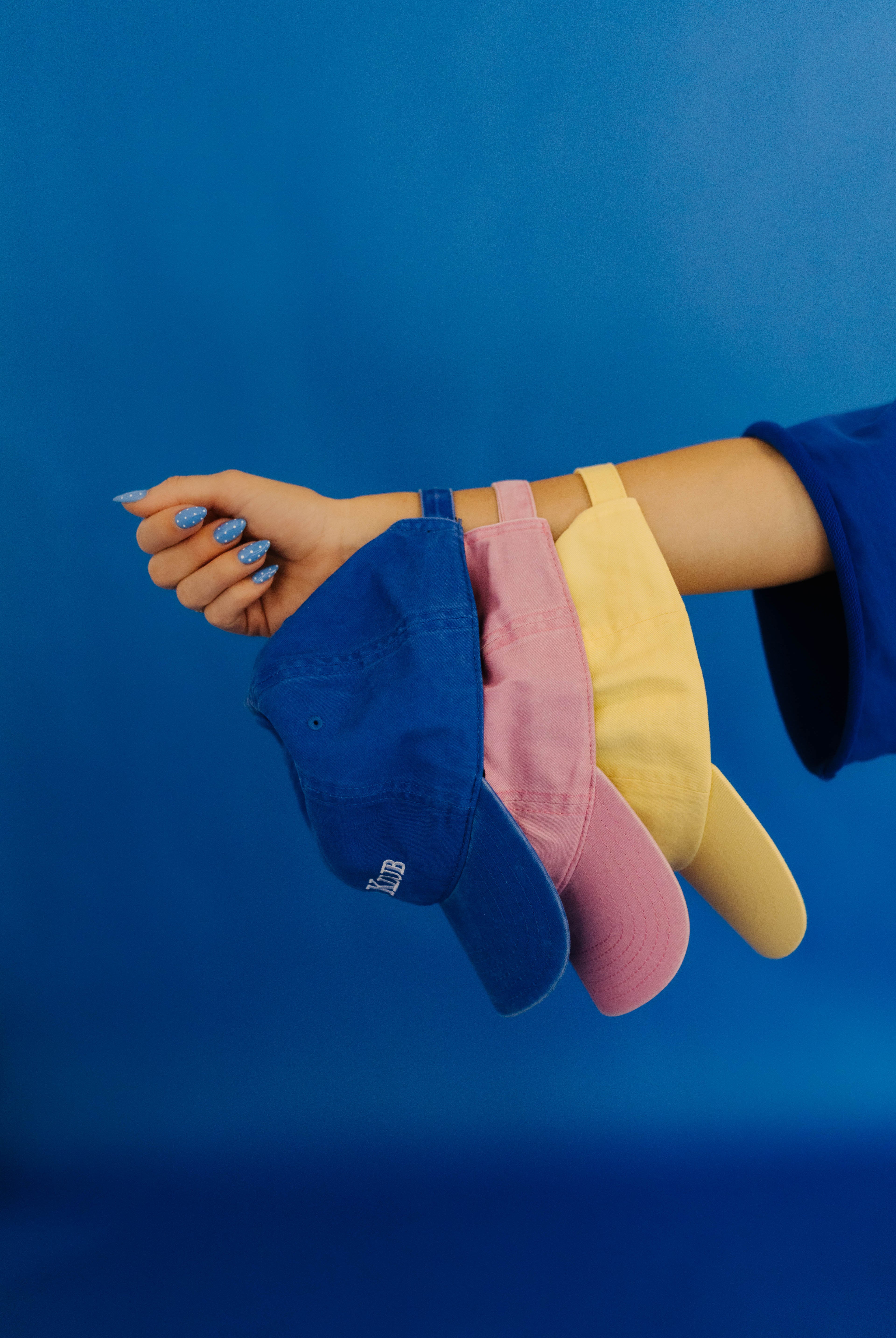 Three colorful caps (blue, pink, yellow) held by a hand against a blue background