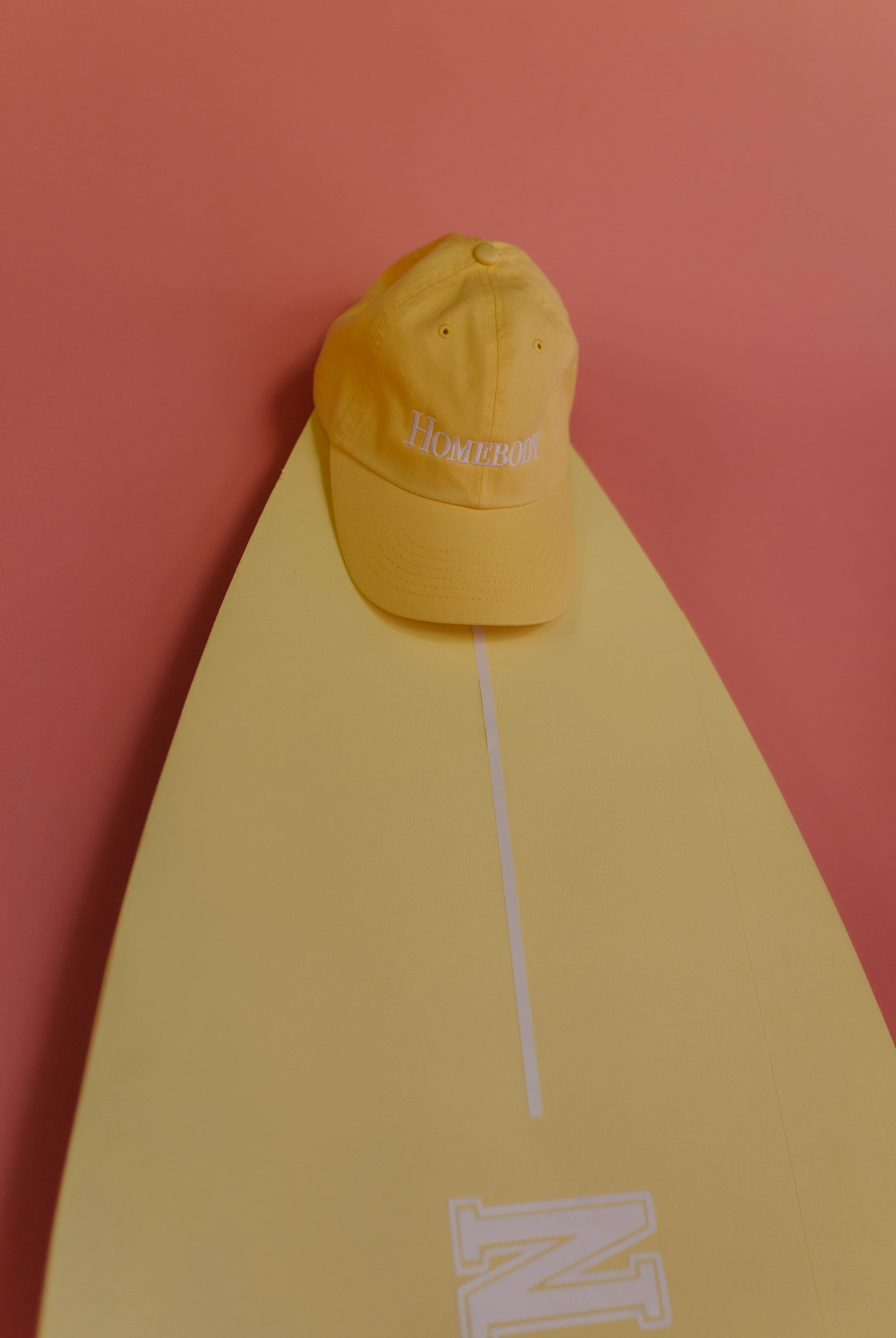 Yellow hat on a yellow surfboard with a pink background