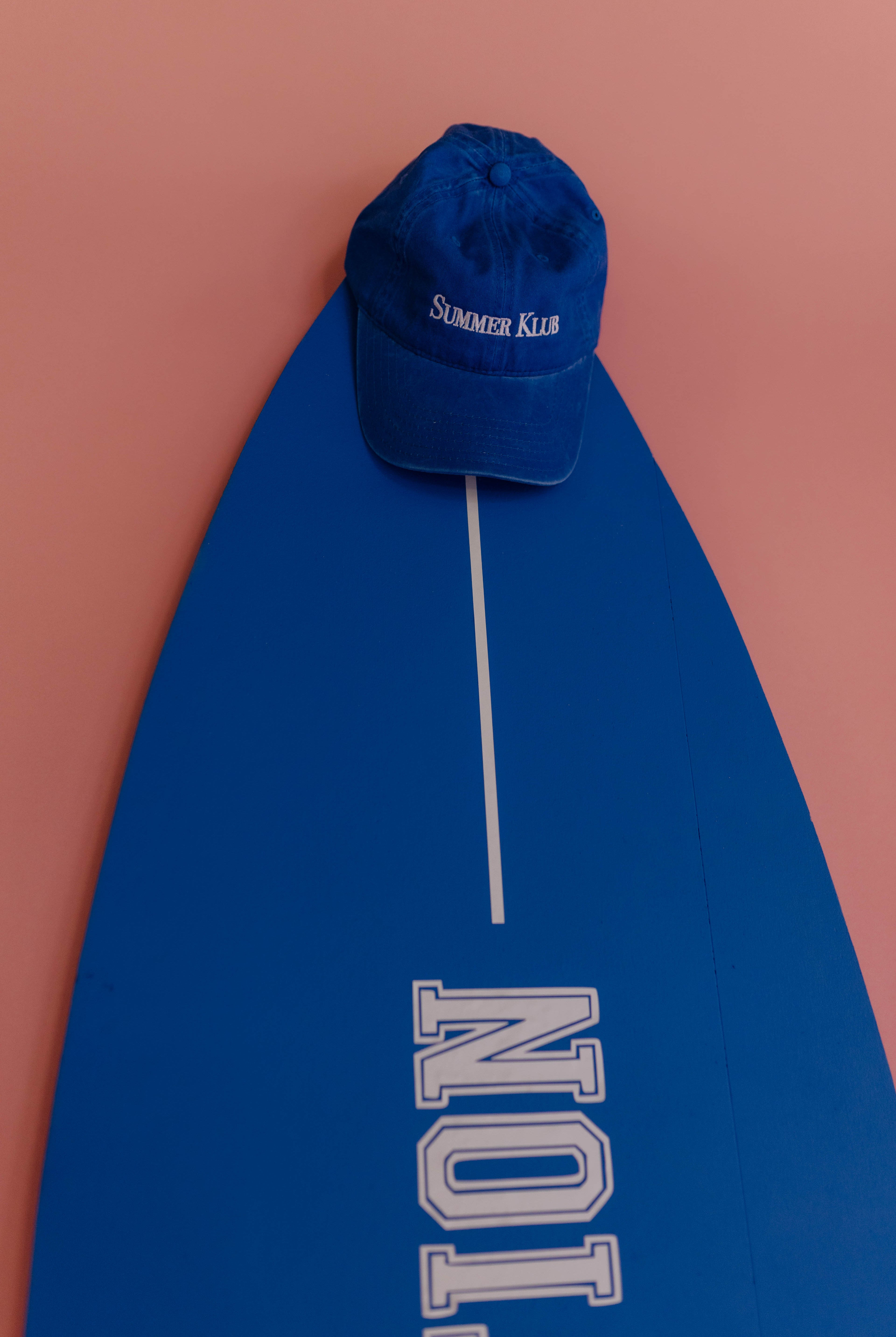 Blue cap on a blue surfboard with 'Summer King' text against a pink background