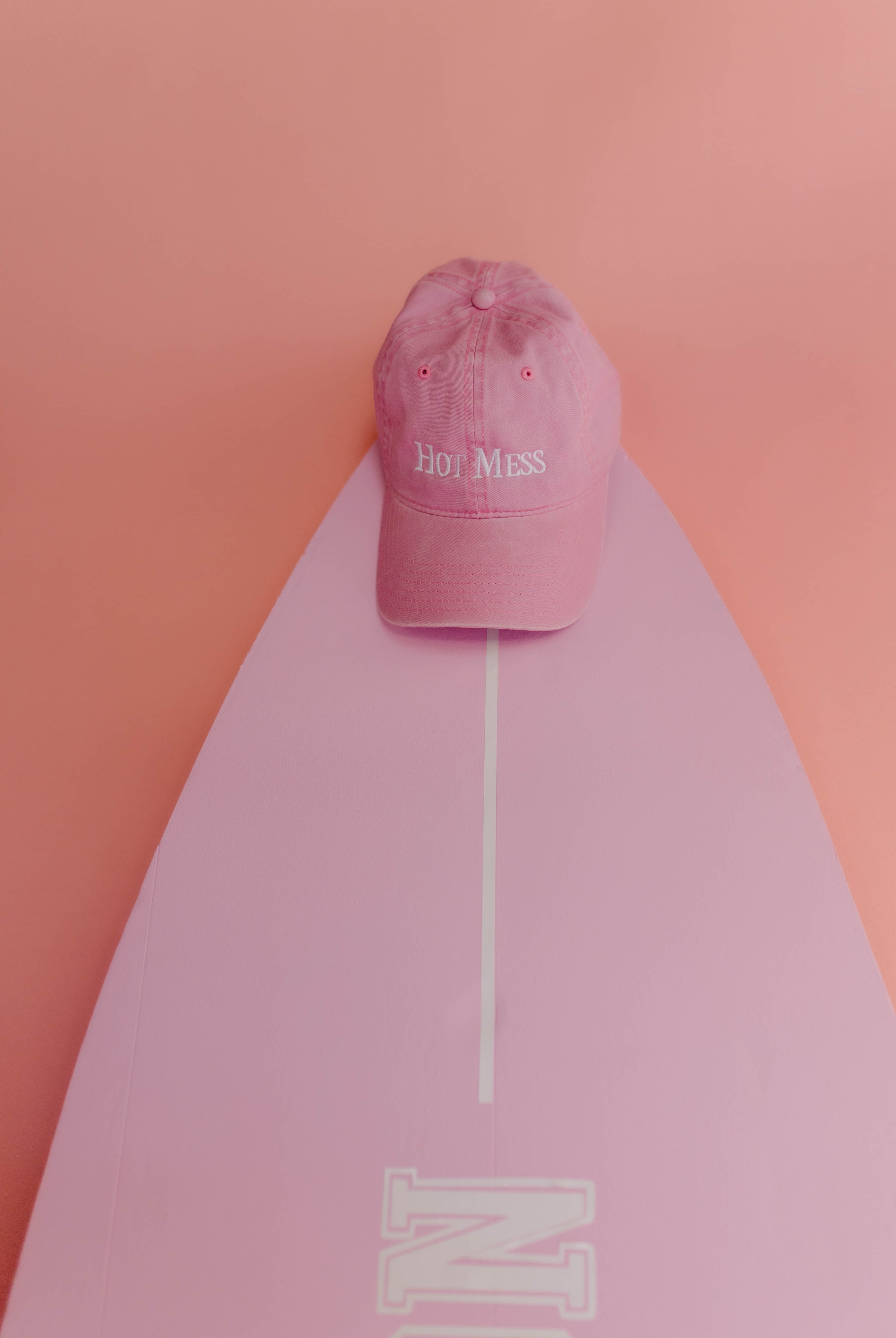 Pink cap with 'Hot Mess' text on a pink surfboard against a pink background