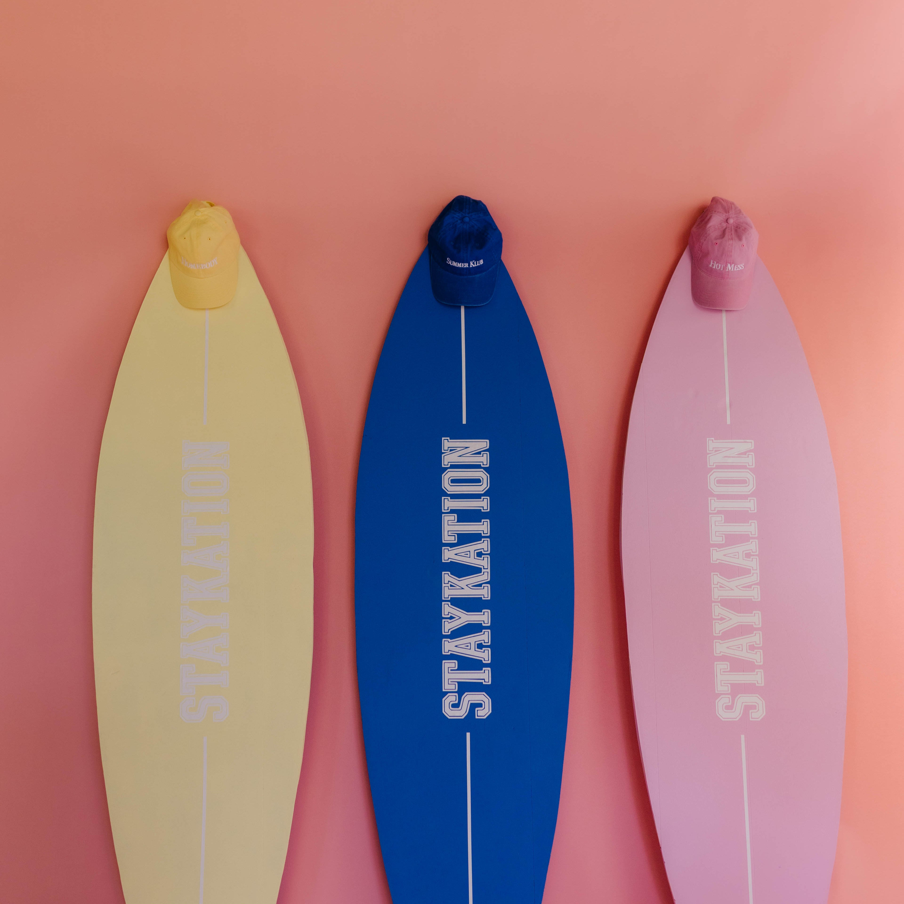 Three surfboards with 'STAYKATION' branding on a pink background