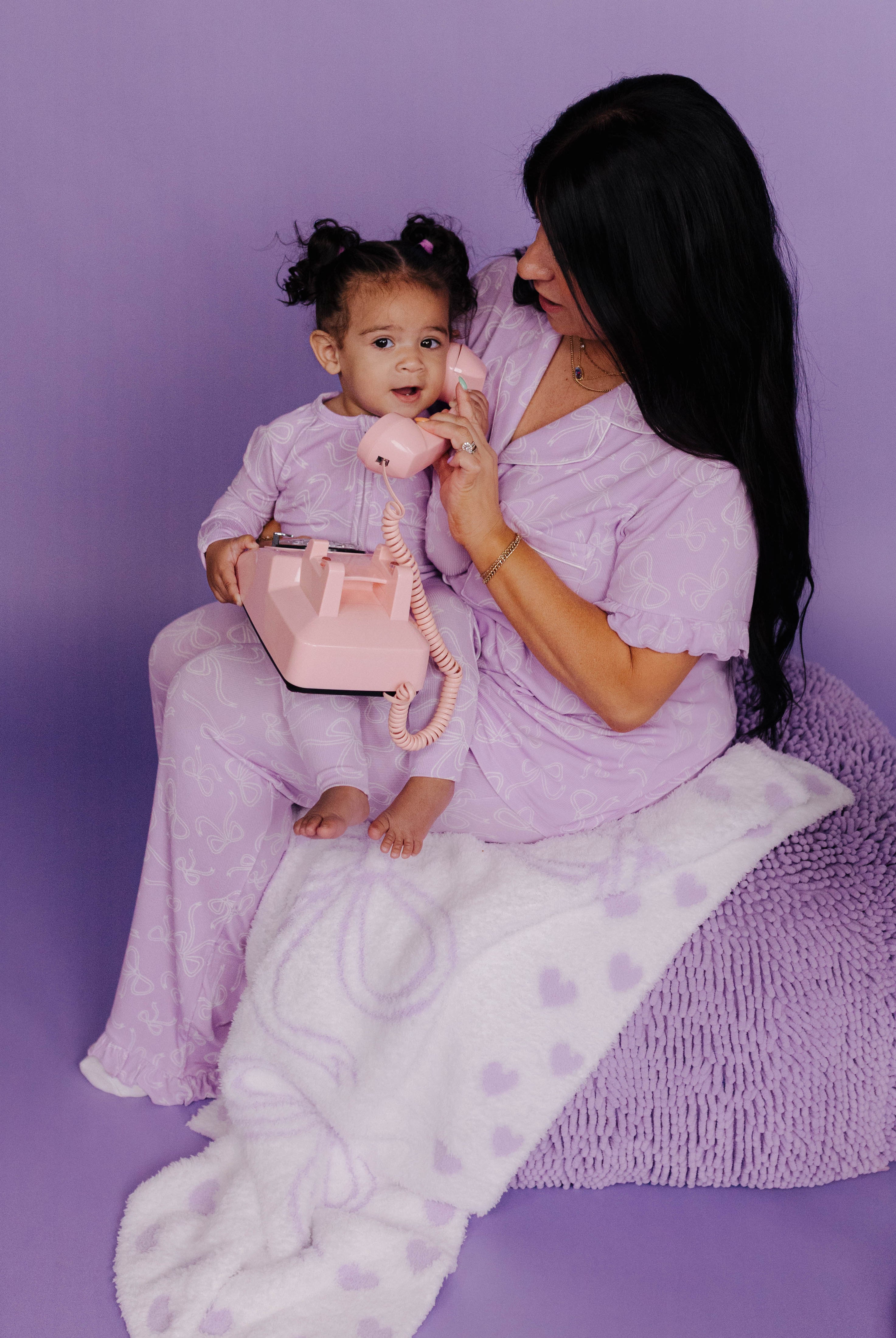 Woman and child in matching lavender pjs sitting on a purple couch with a pink toy.