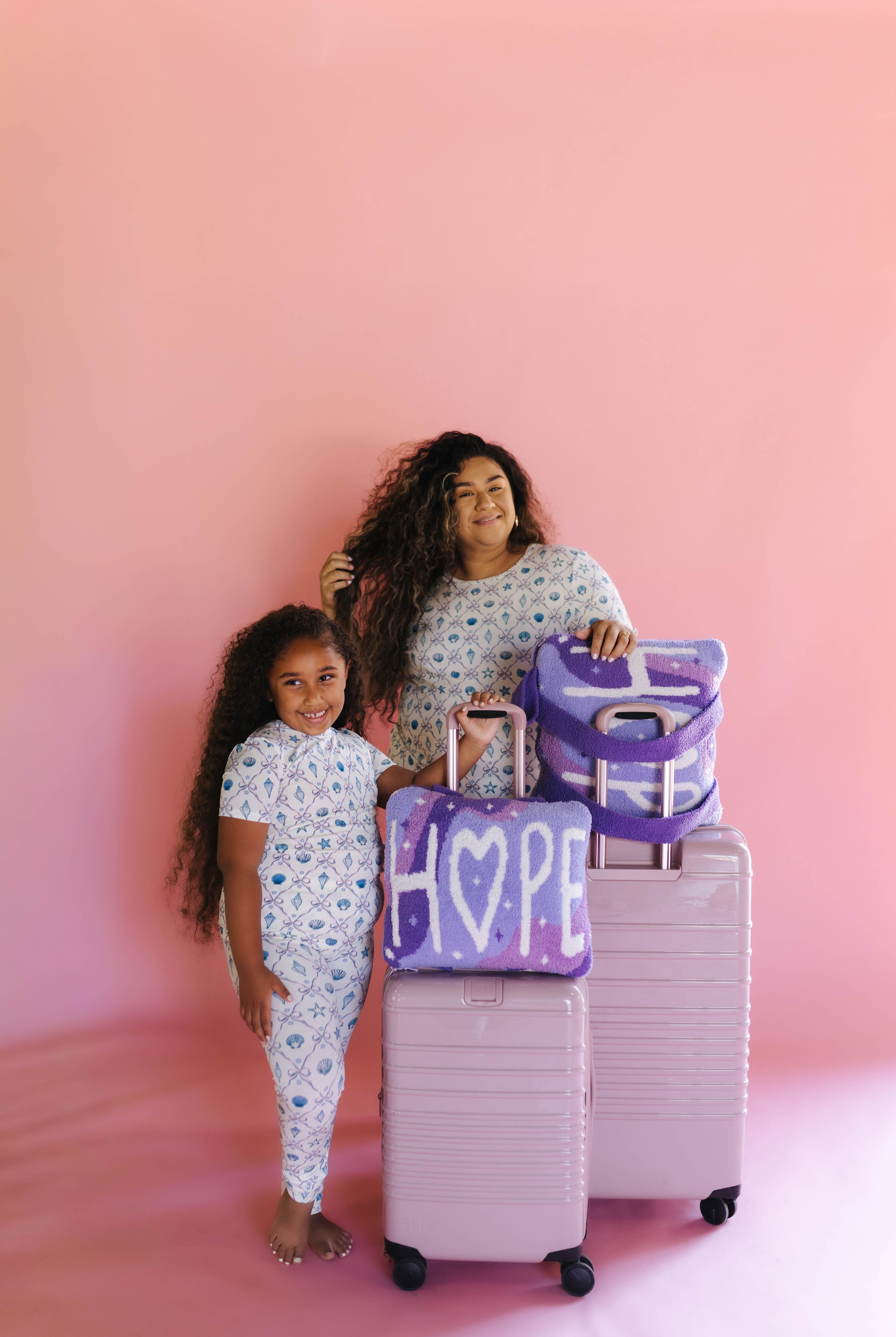 A woman and a young girl wearing matching pjs holding matching suitcases with the matching quillows that say hope